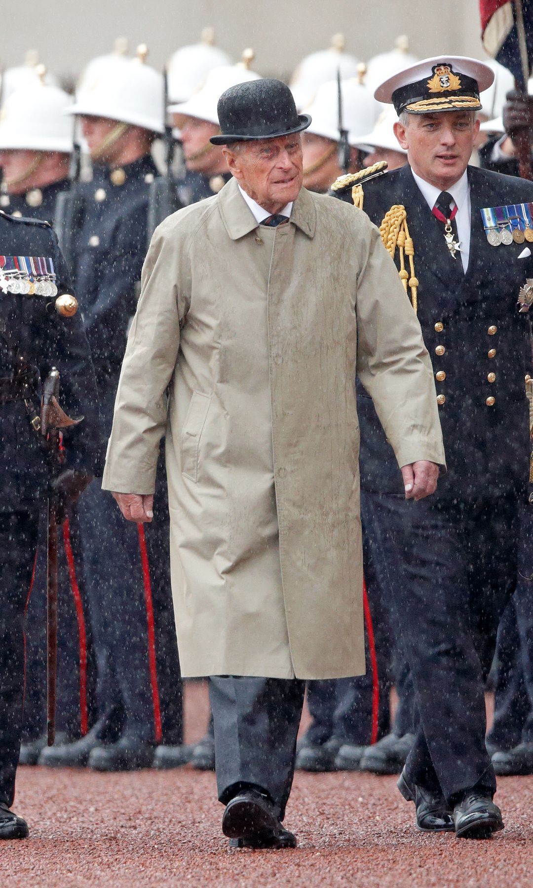 El Príncipe Felipe, Duque de Edimburgo, camina bajo la lluvia con oficiales militares.