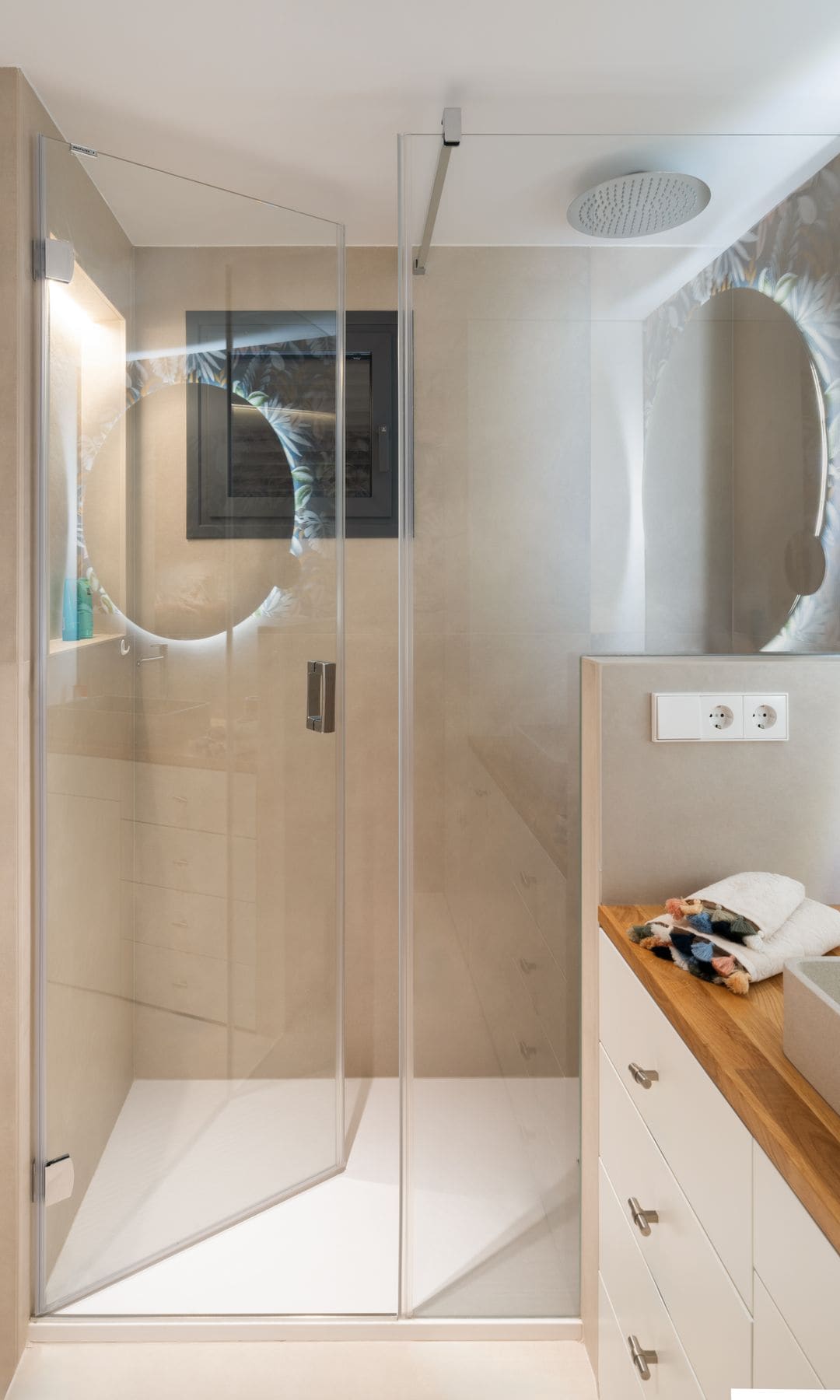 Baño con ducha, mampara casi sin perfiles, hornacina en la ducha con luz, mueble blanco con encimera de madera, paredes y suelos de mármol crema
