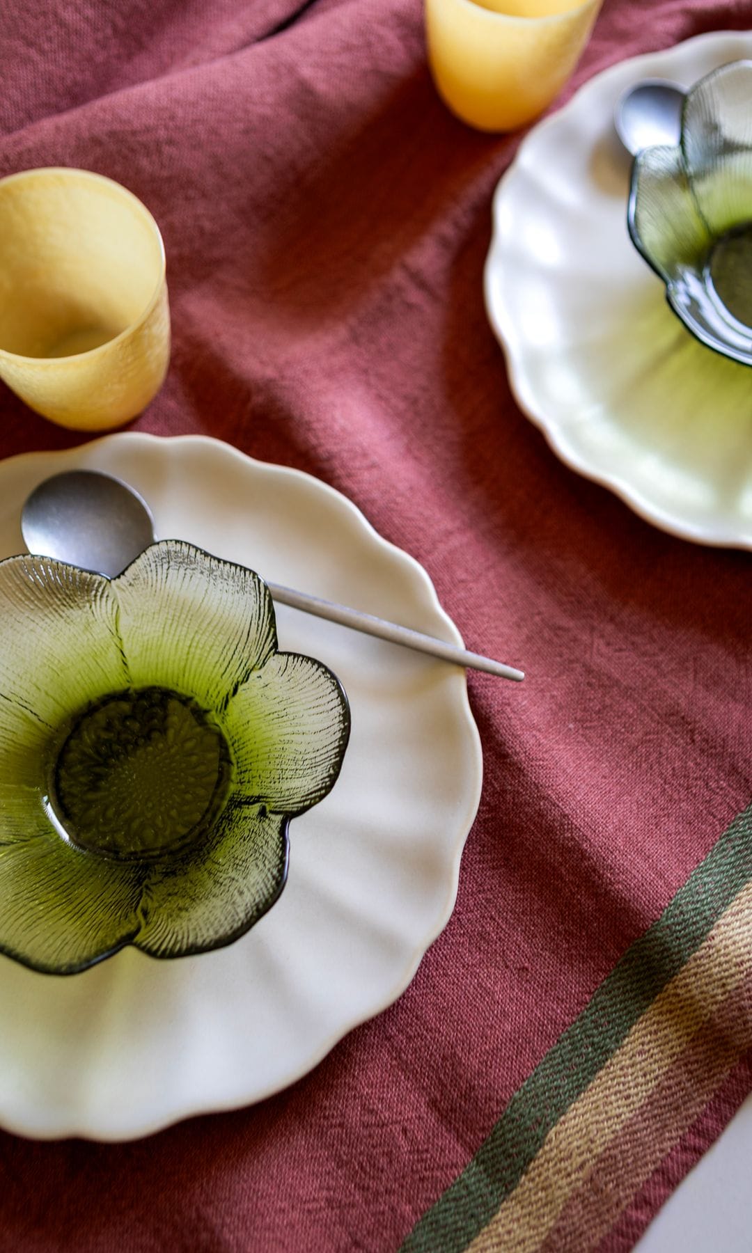 Mantel burdeos con cenefa, platos blancos, cuencos de cristal verde, vasos amarillos 