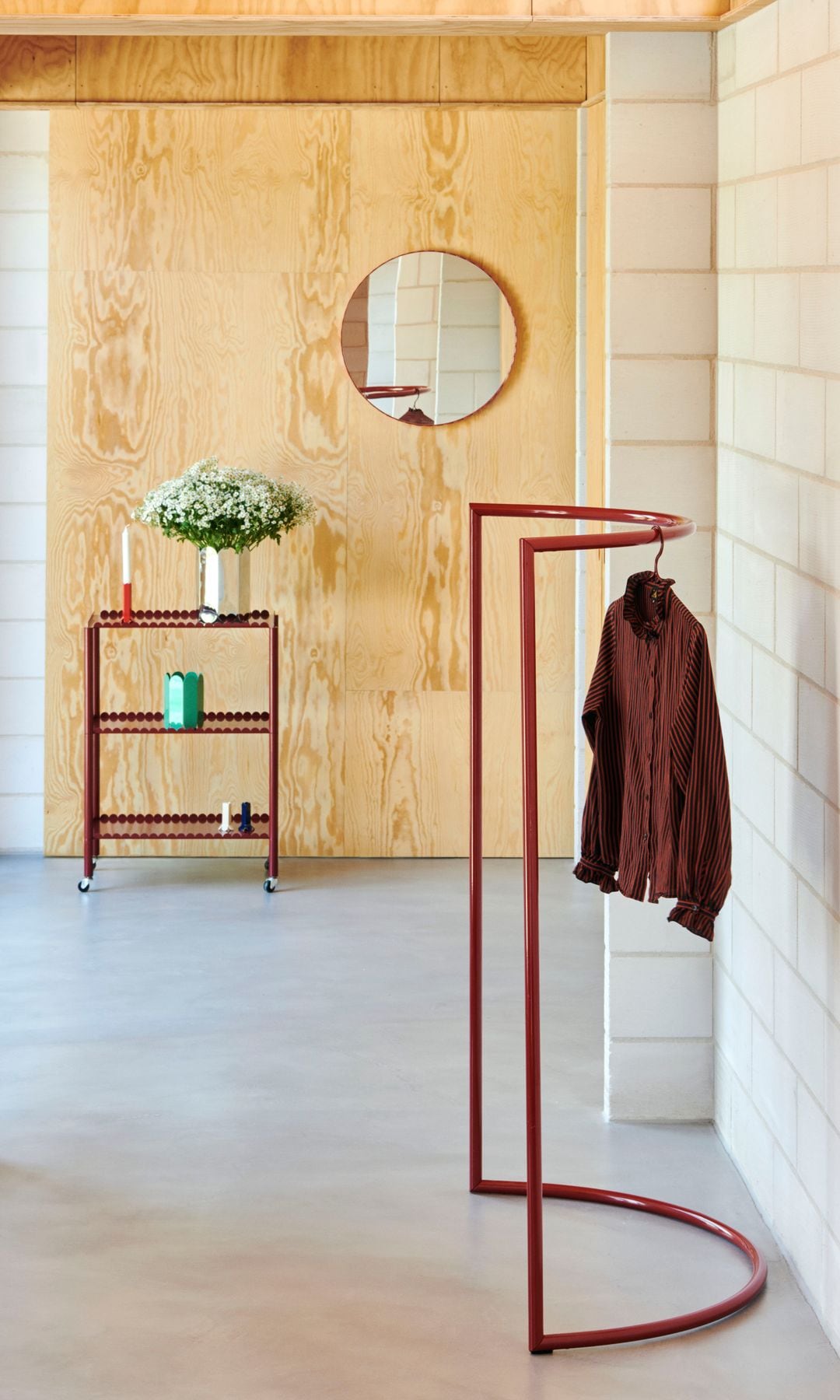 Perchero de suelo rojo y de forma curva, paredes de madera, carrito rojo con ruedas