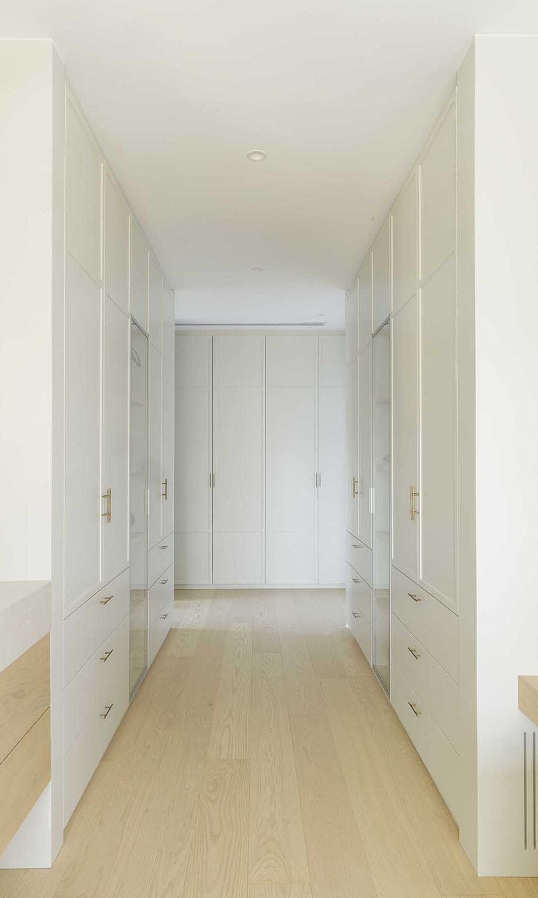 Vestidor con armarios blancos hasta el techo, suelo de madera