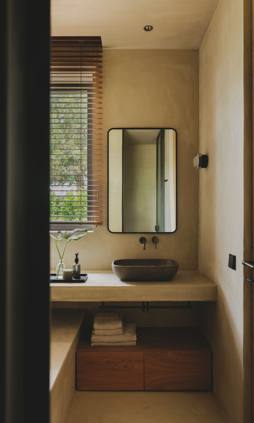 Baño con encimera de piedra, espejo, estor de lamas de madera, mueble de lavabo de madera, espejo sobre la encimera, bañera