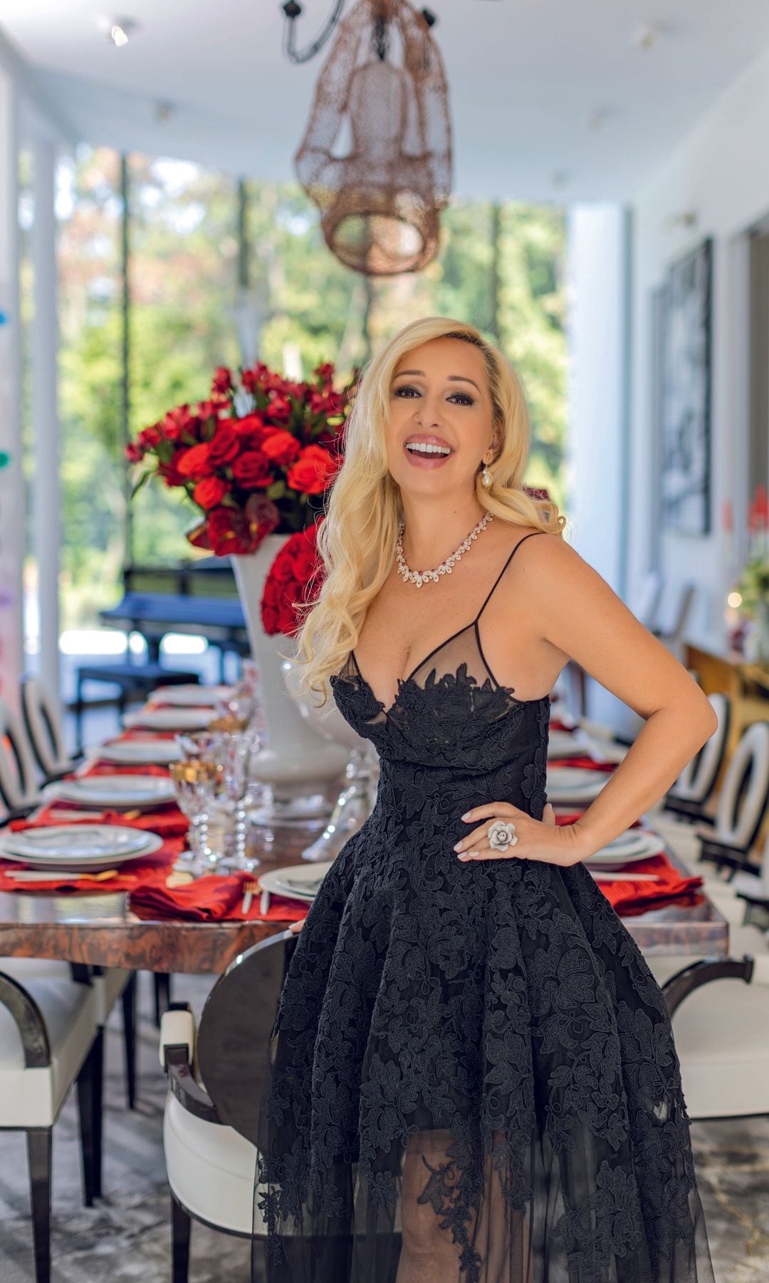 Monique Delacroix con vestido negro y collar de perlas en comedor elegante.