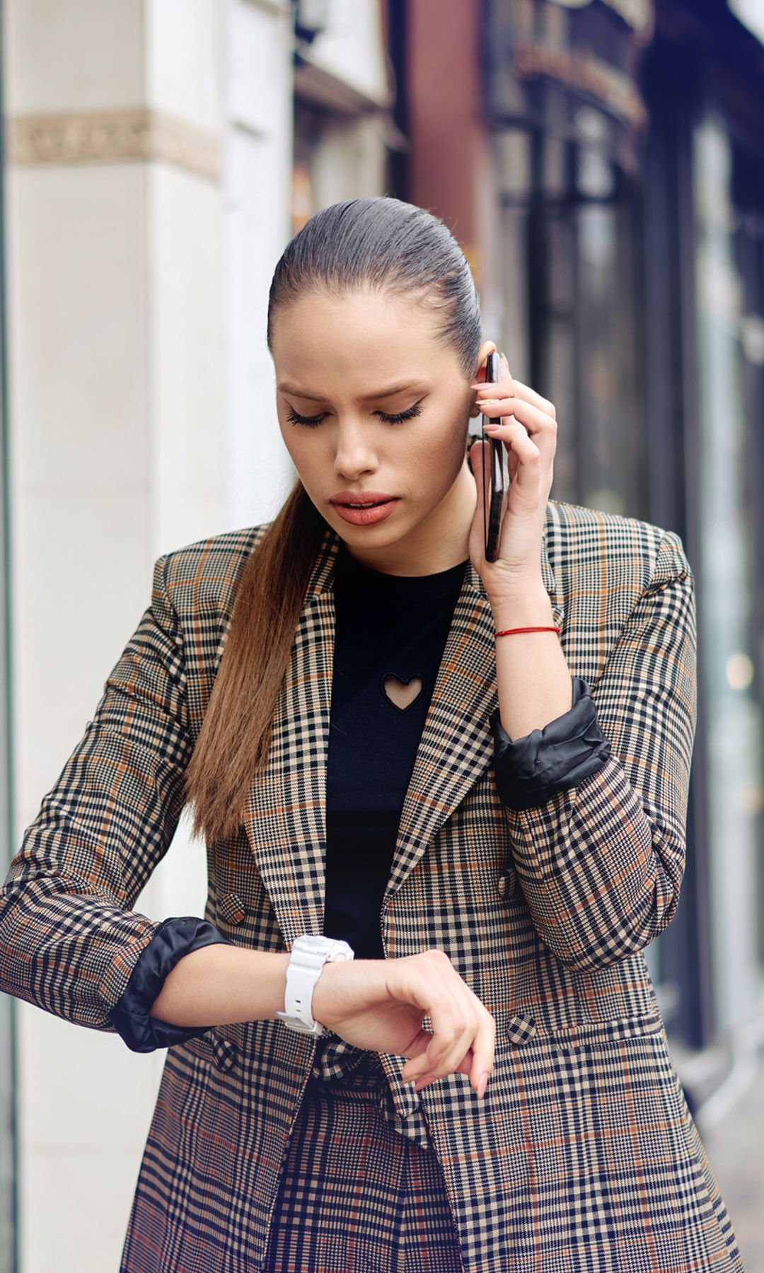 Mujer preocupada y estresada chequeando su reloj mientras habla por teléfono