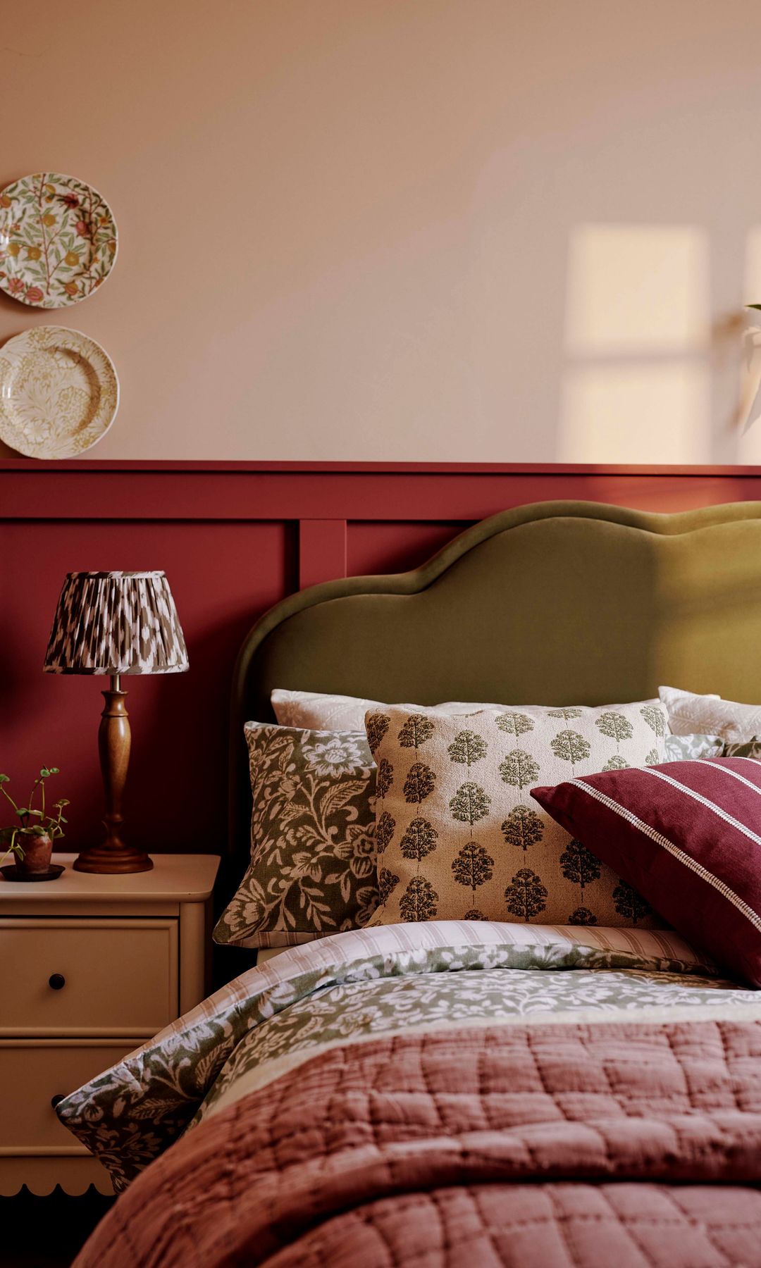 Dormitorio con cabecero tapizado, zócalo alto de madera en color burdeos, platos en la pared del cabecero, ropa de cama de flores