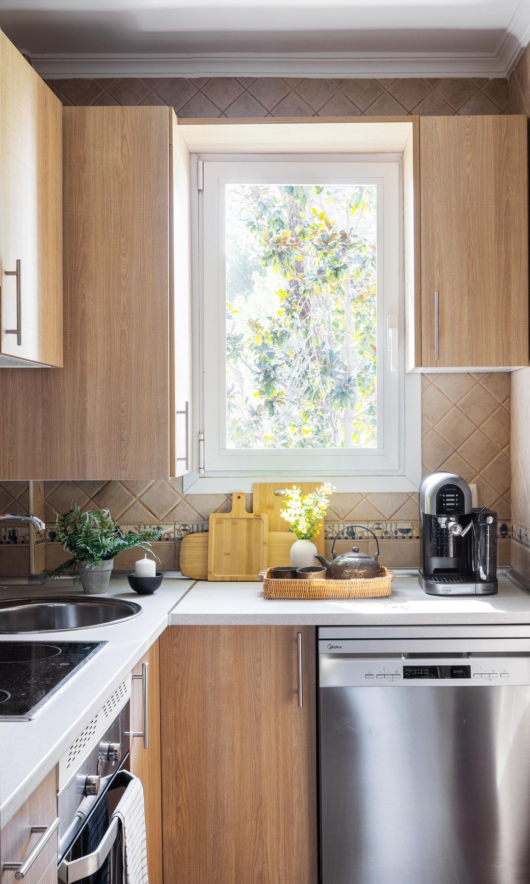 Cocina estrecha con muebles de madera, lavavajillas metálico, ventana