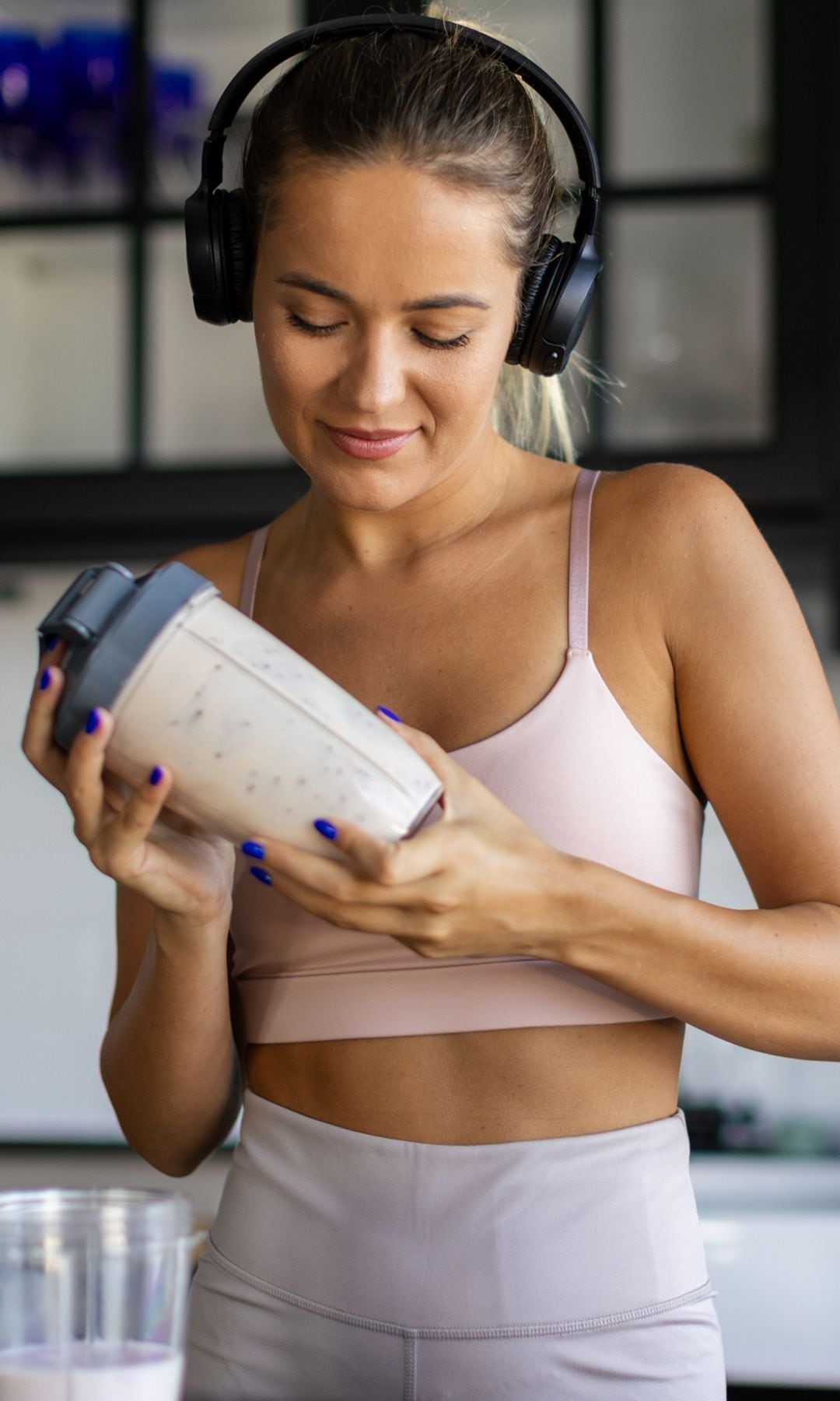 Una chica joven vestida de deporte preparándose un batido para comer