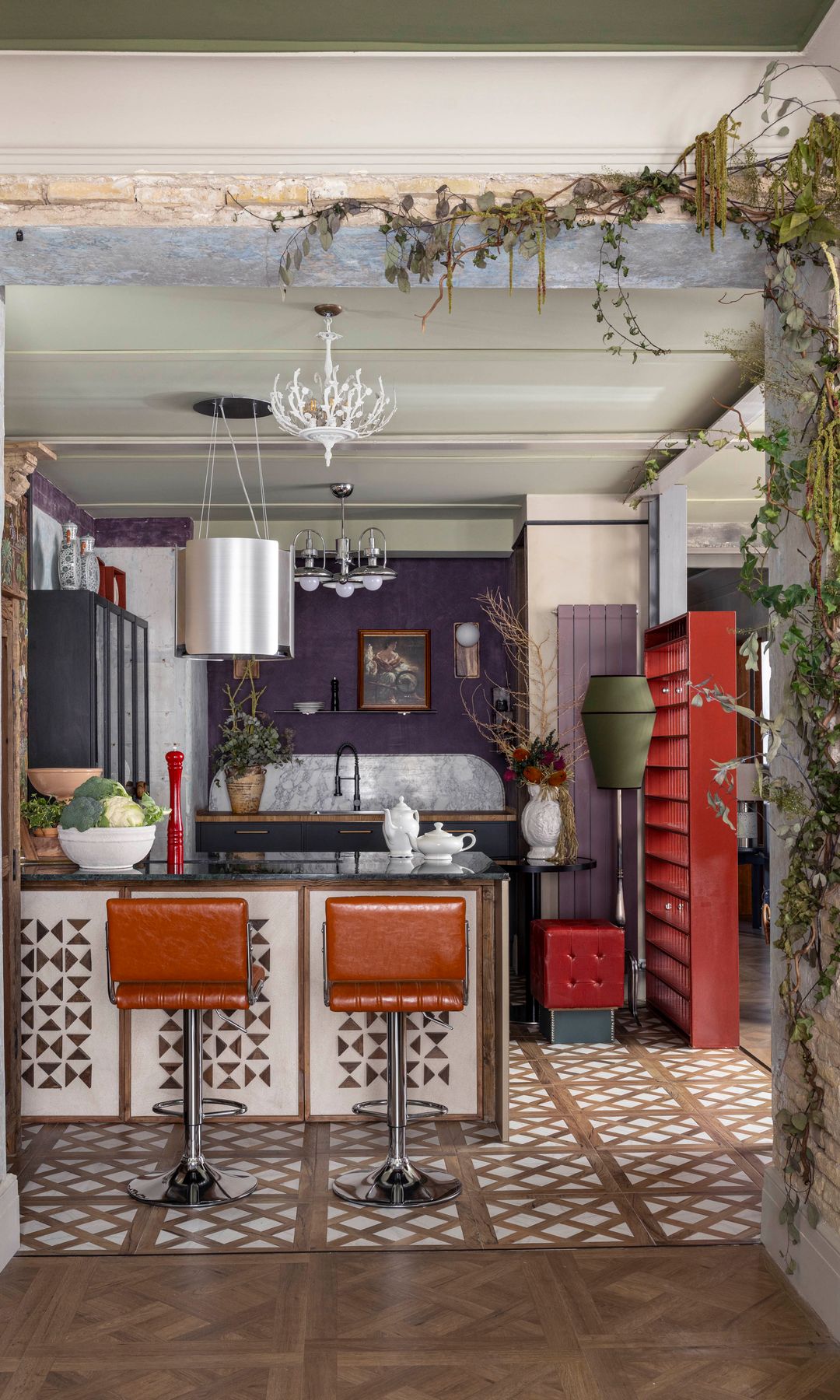 Cocina abierta con península, estantería roja, paredes moradas, suelo de baldosas en marrón y blanco, taburetes altos de cuero, armarios de cocina negros 