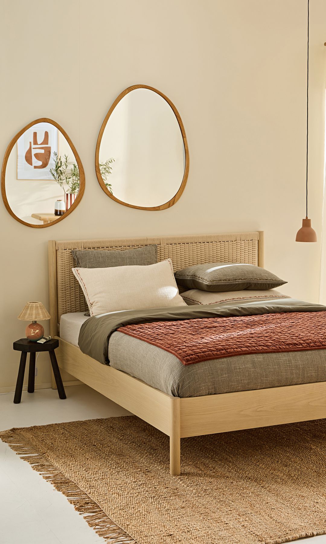 Dormitorio con cama de madera con el cabecero de rejilla, alfombra de fibras vegetales, espejos de formas curvas sobre la cama, lámpara de techo, taburete negro