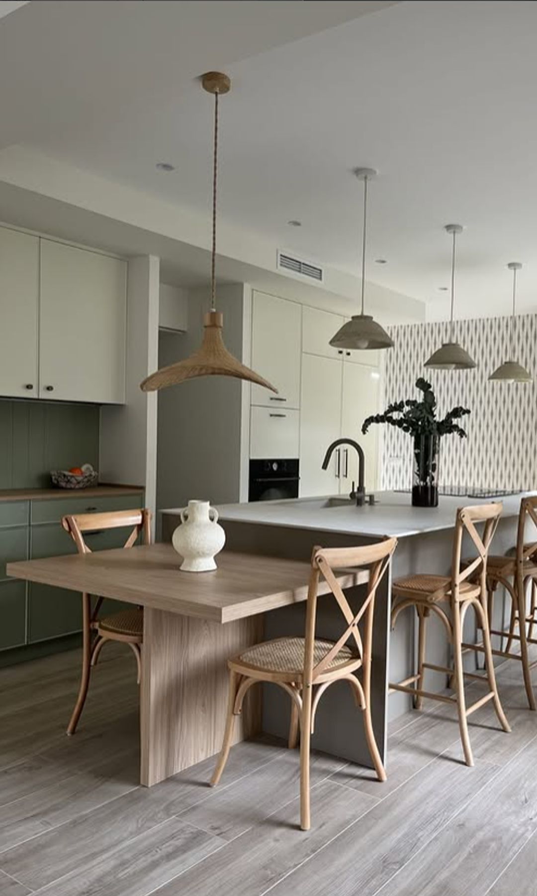 Cocina con isla y mesa de cocina adosada en madera, alacena de color verde, muebles de color verde claro, sillas de madera
