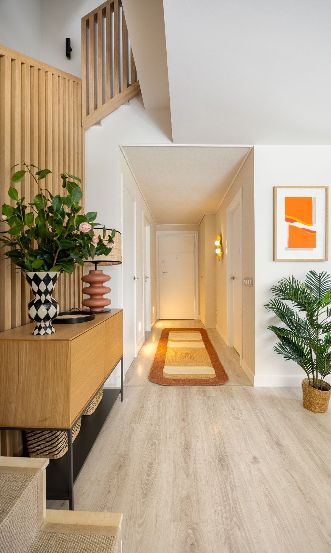 Pasillo con recibidor abierto, alfombra, apliques en la pared y planta alta en el suelo