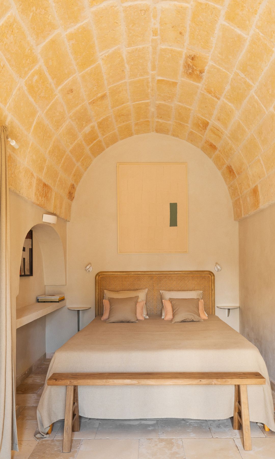 Dormitorio bajo bóveda con cabecero de rejilla y banqueta de madera a los pies de la cama, hornacina con balda
