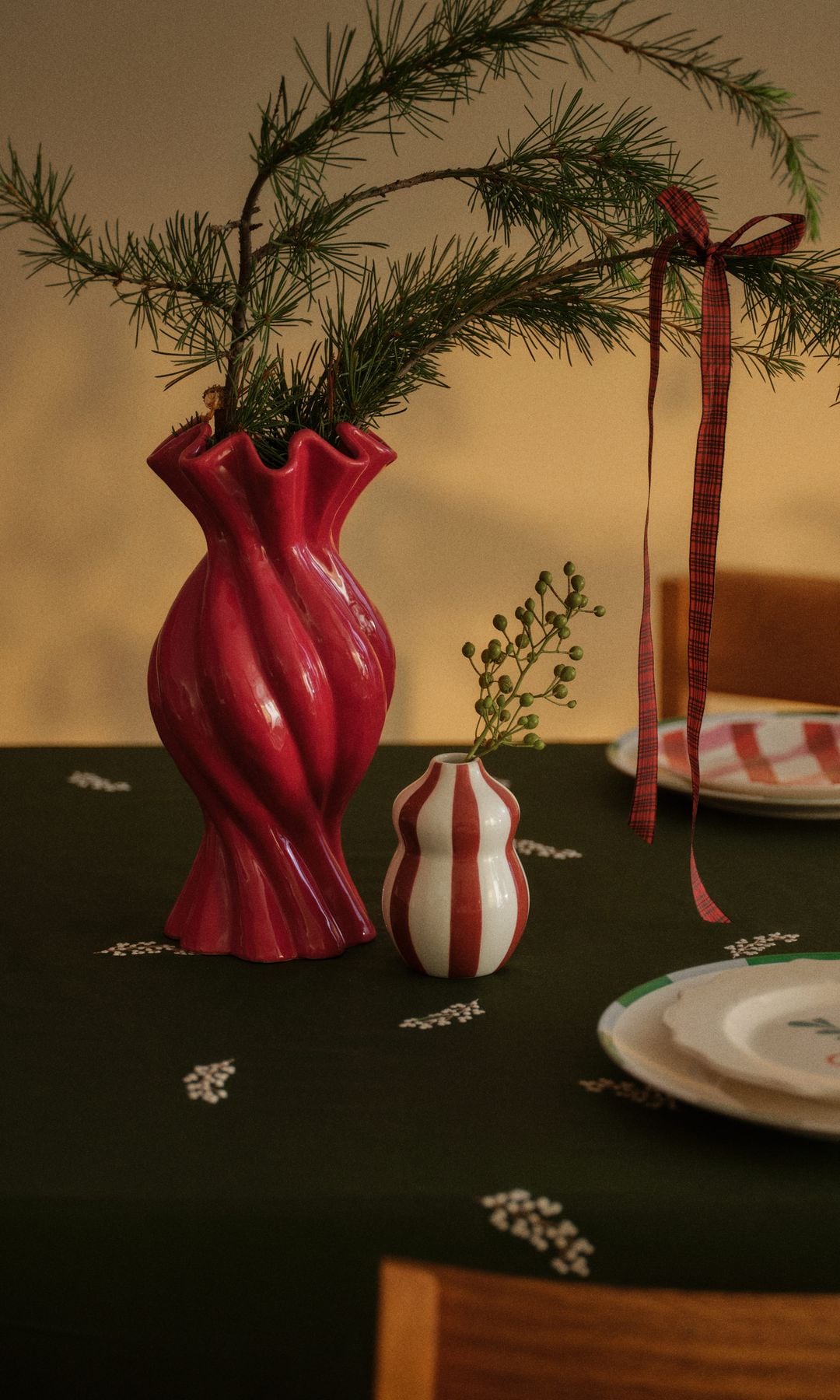 Mesa de Navidad con mantel verde, vajilla blanca, centro de mesa con jarrón rojo, ramas de abeto 