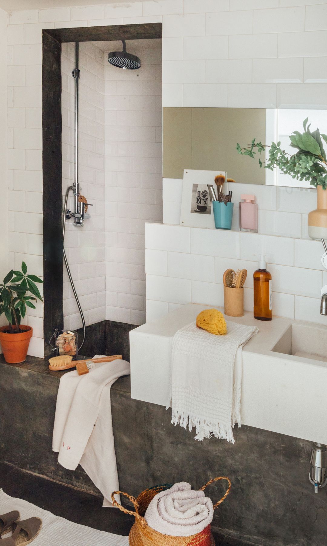 Baño con ducha, lavabo con encimera blanco, azulejos blancos, reúsa de obra, espejo, cesto, plantas