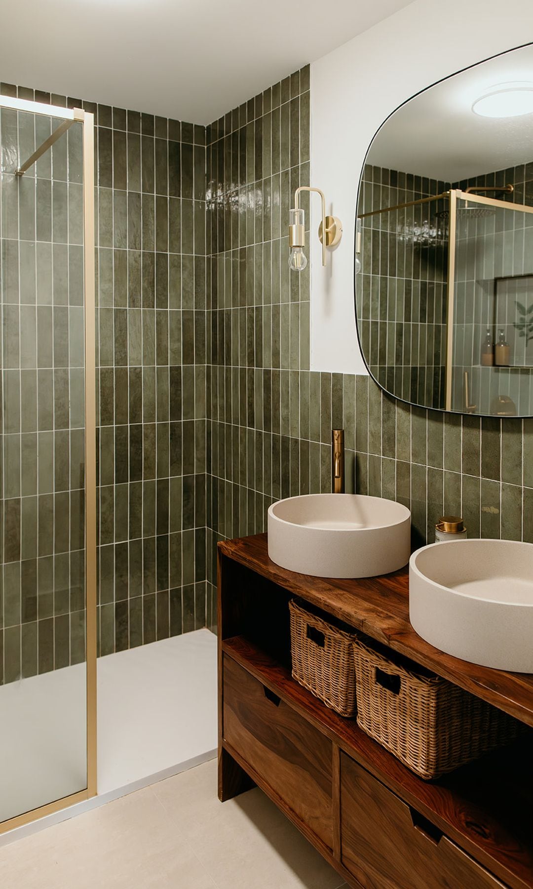 Baño con azulejos verdes, mueble de madera, espejo, mampara, lavabos blancos y cestos
