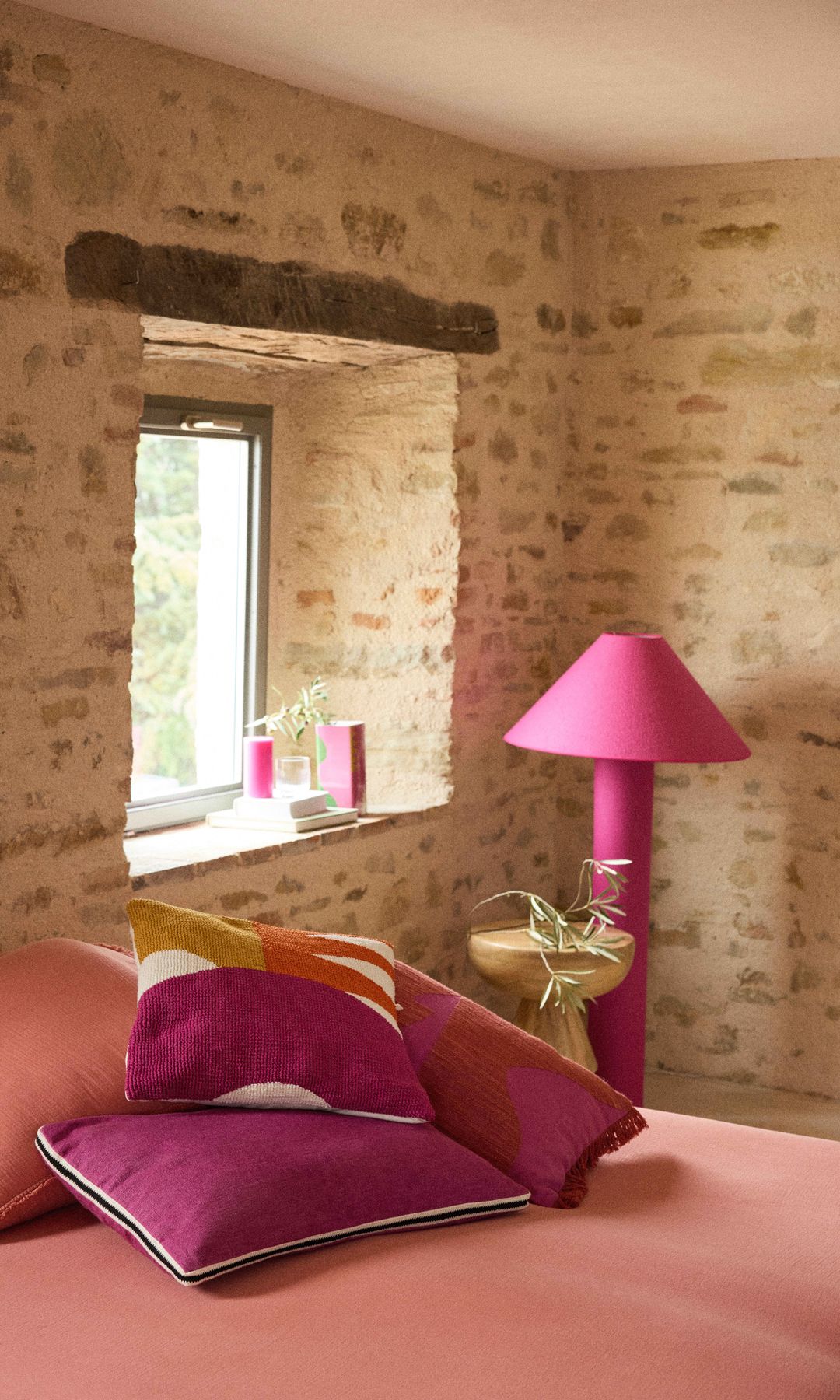Dormitorio rústico con paredes de ladrillo enlucido, ropa de cama rosa salón, cojines y lámpara de pie rosa fucsia