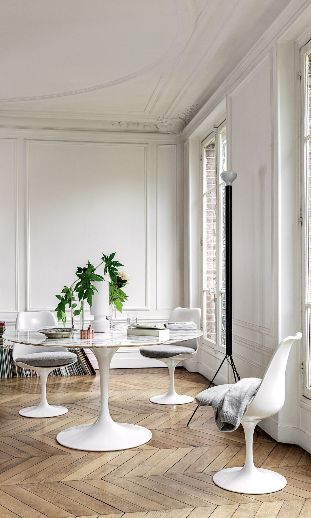Comedor con mesa y sillas Tulip en color blanco, suelo de madera en espiga, molduras en las paredes y salida al balcón 