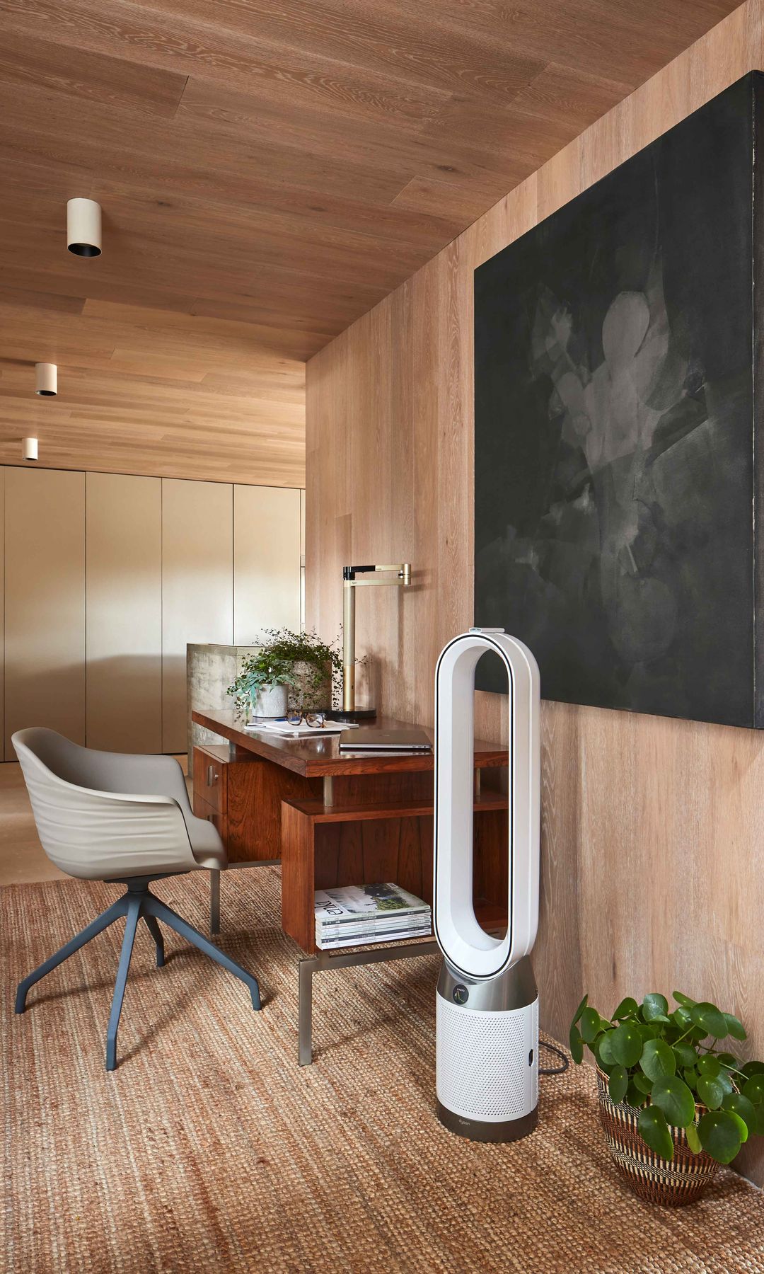 Despacho con plantas y purificador Dyson de pie, mesa de madera oscura, cuadro en la pared
