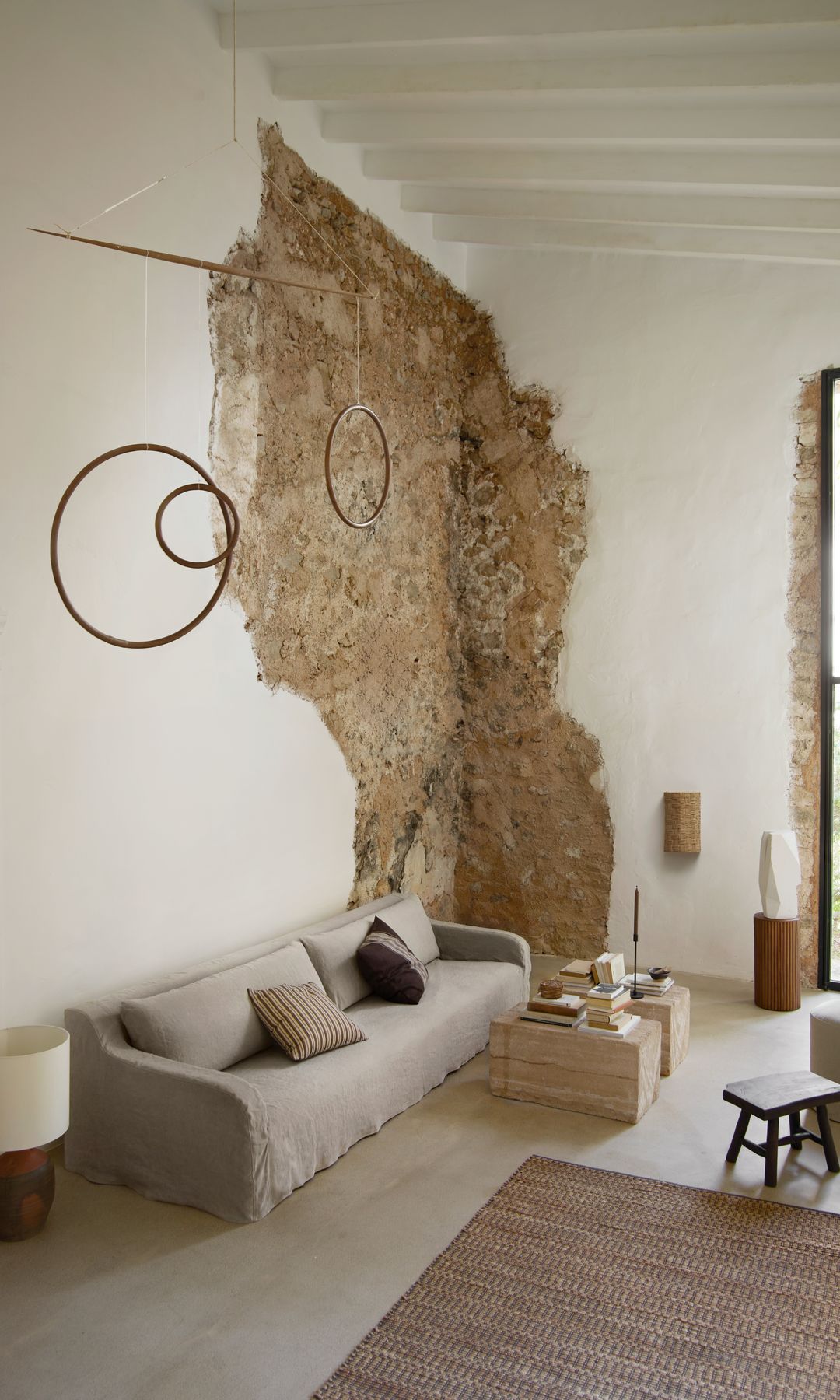 Salón con pared de piedra, sofá con funda gris, lámpara de techo escultura, mesa de centro de mármol