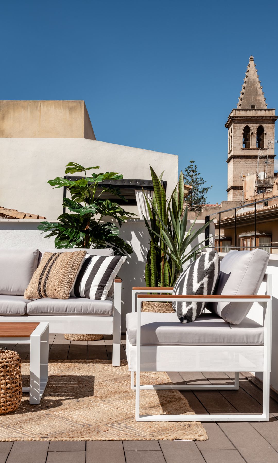 Terraza en azotea con muebles blancos, alfombra de fibras vegetales, farolillo de fibras. plantas
