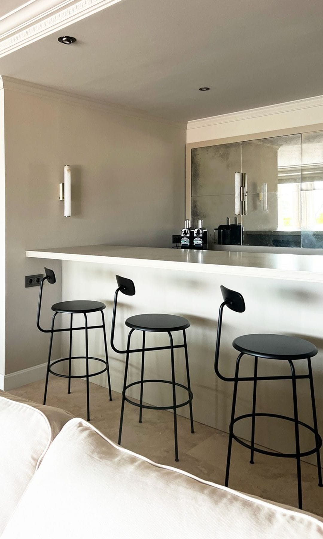 Cocina blanca abierta al salón con isla con taburetes negros y sofá blanco