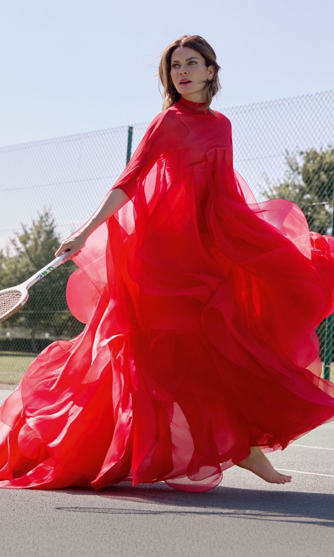 En una imagen cargada de teatralidad, nuestra protagonista salta a la cancha de tenis con vestido efecto capa, de organza roja, con volantes y cuello alto, de la colección de alta costura de Stéphane Rolland