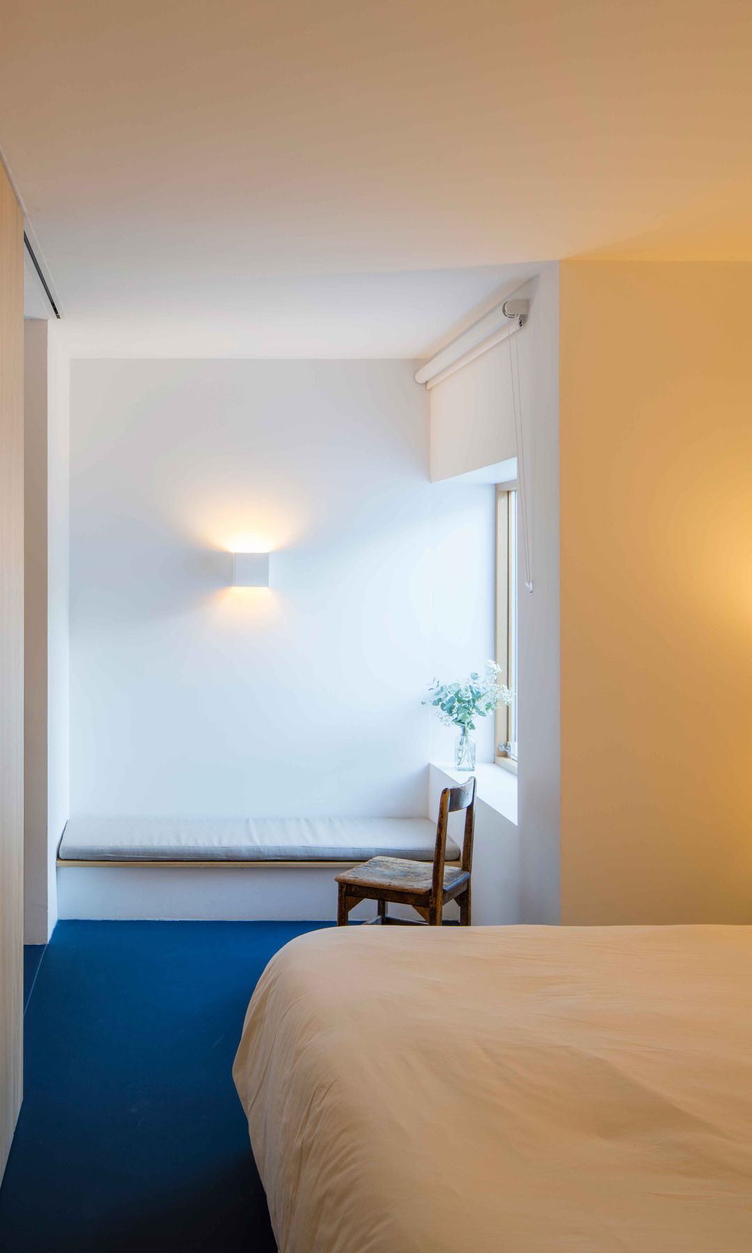 Dormitorio con suelo azul, puertas de madera, ropa de cama blanca, rincón lectura