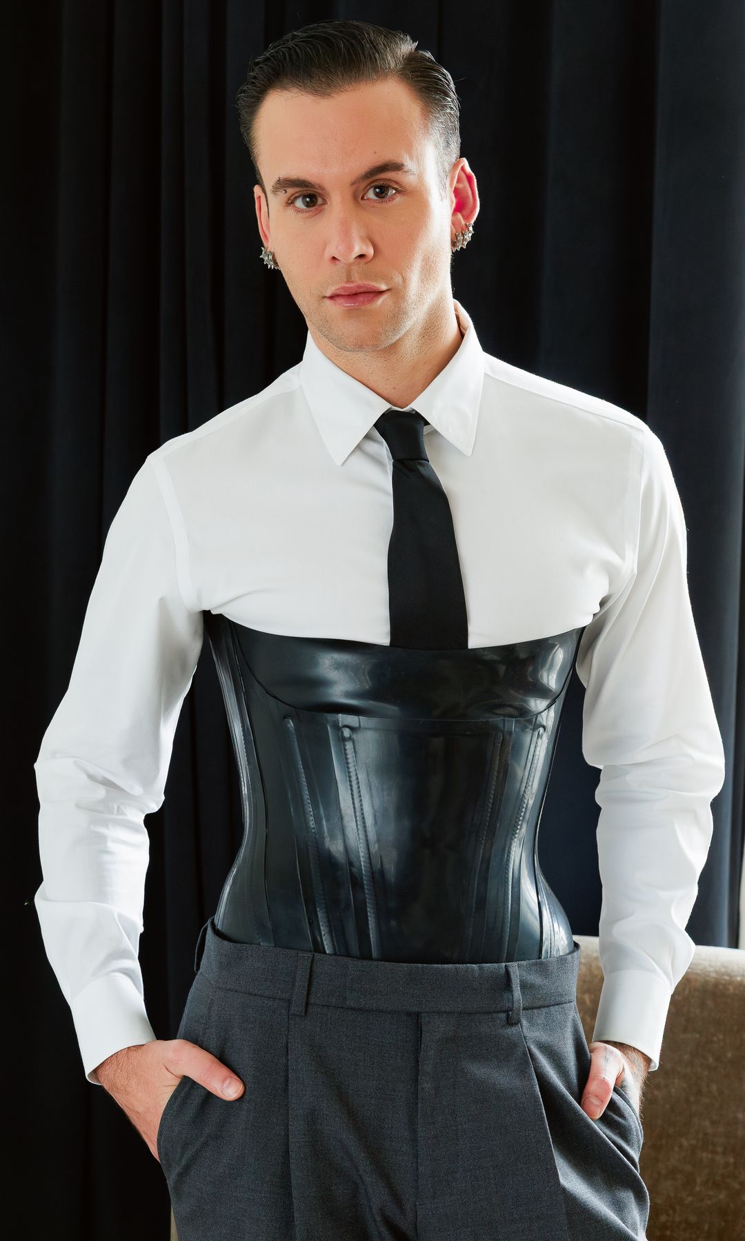 Luis Javier con camisa blanca, corsé negro y traje gris, manos en los bolsillos