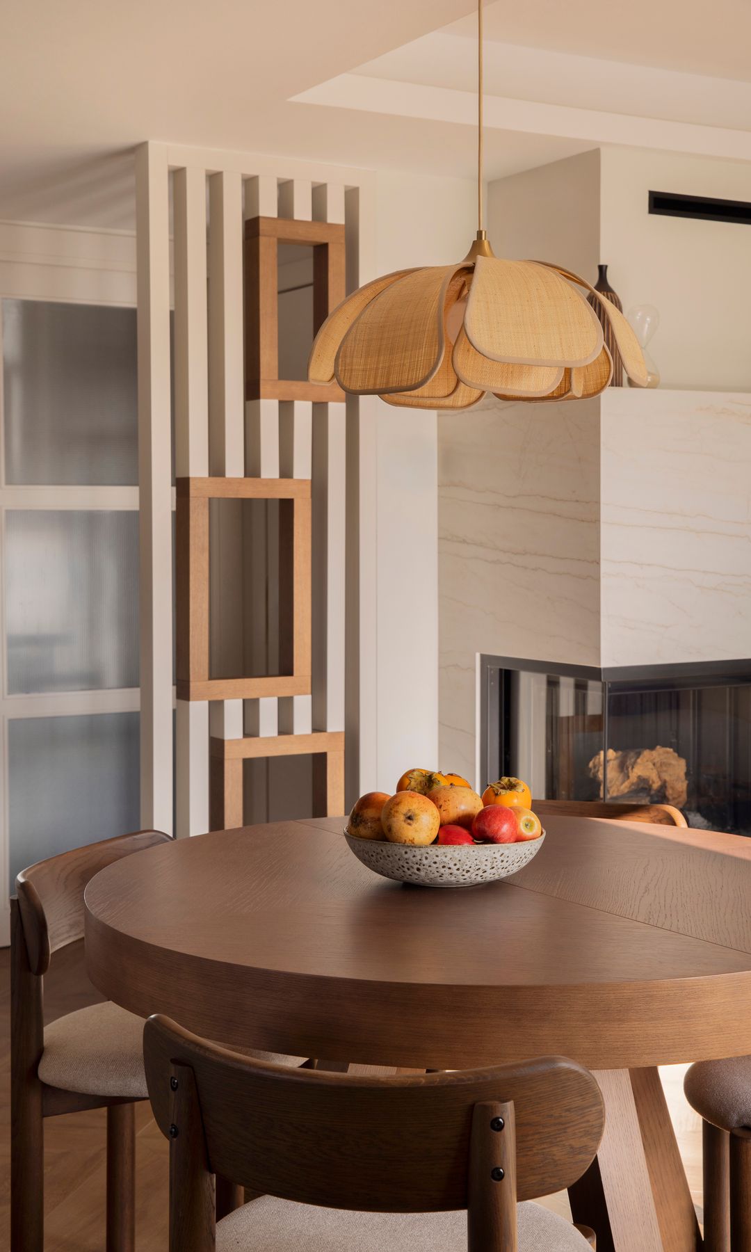 Comedor con mesa redonda de madera oscura, lámpara de techo de fibras vegetales, frutero, sillas de madera oscura con asiento tapizado