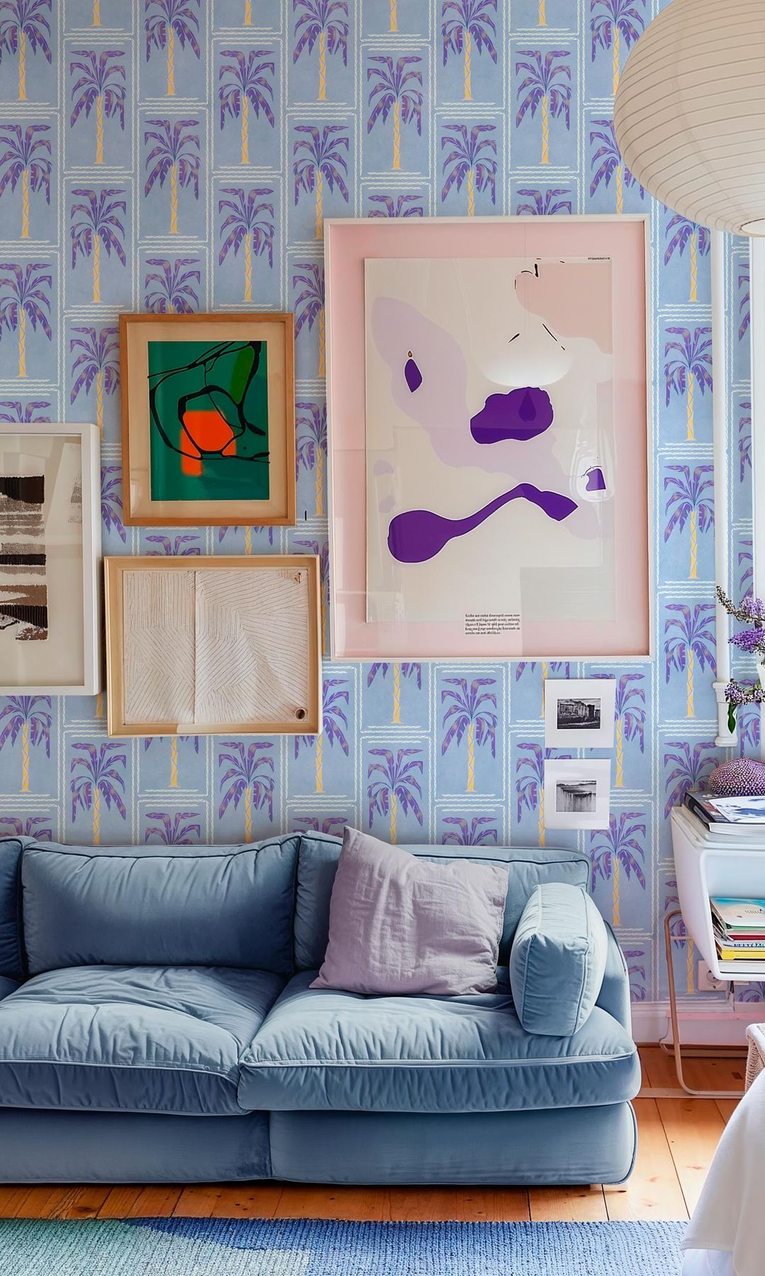 Salón con papel pintado azul con estampado, cuadros en la pared del sofá, sofá de color azul claro, lámpara de papel 