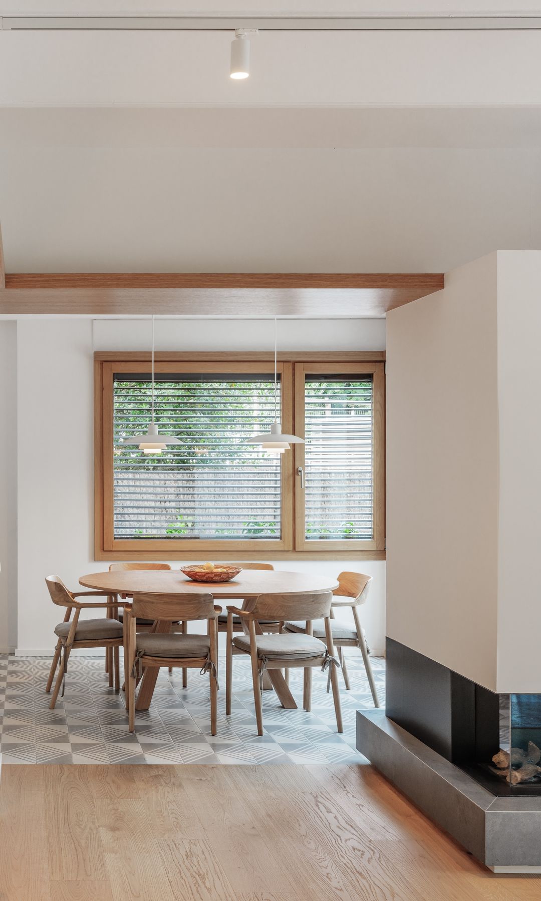 Comedor abierto a la cocina con chimenea, mesa redonda, ventana de madera, suelo de baldosas grises, suelo de madera
