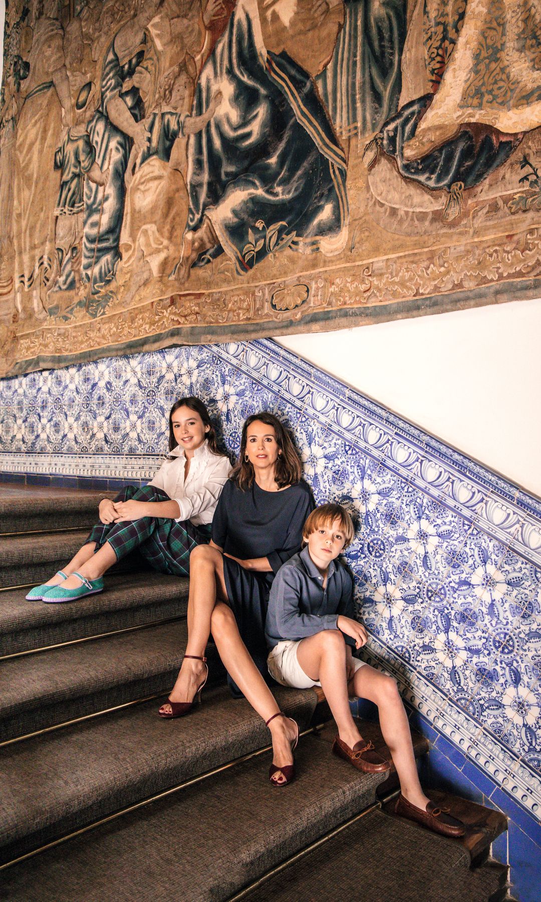 María Martín Candela y sus hijos, Lola y Diego, en la escalera, en la que destaca el friso de azulejos antiguos (que decora también la embocadura de la chimenea) y un tapiz de escuela flamenca del siglo XVI