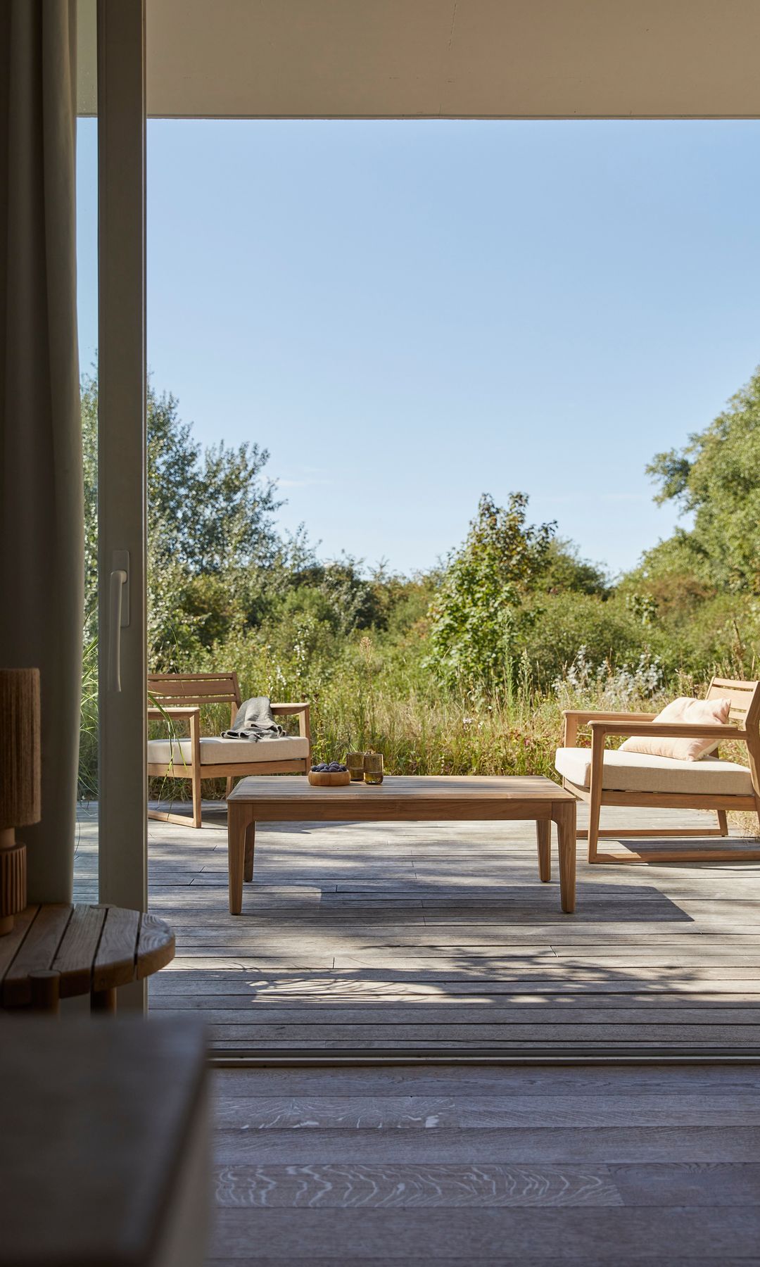 Salón exterior rodeado de naturaleza, ventanal que comunica con el salón de dentro de casa