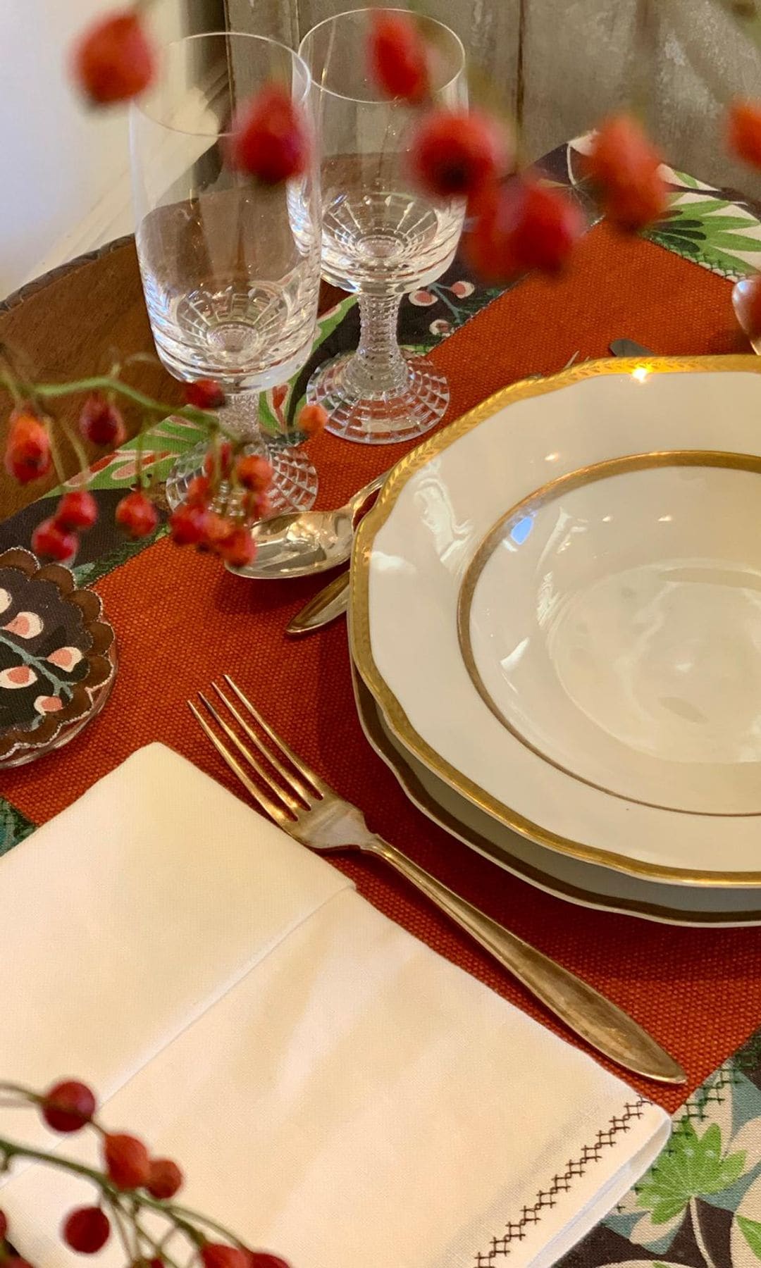 Mesa de Navidad con mantel individual rojo, copas, arreglo floral, vajilla blanca con el filo dorado