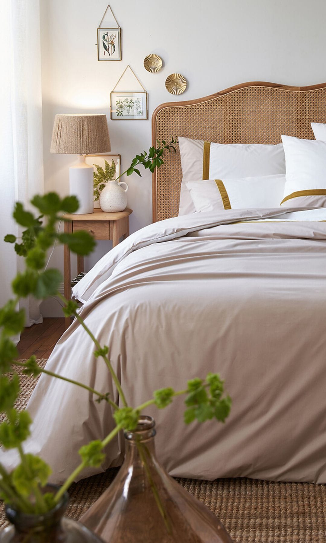 Dormitorio con cabecero de rejilla, plantas y flores, ropa de cama blanca, alfombra de fritas vegetales, lámpara de sobremesa con la pantalla de fibras vegetales