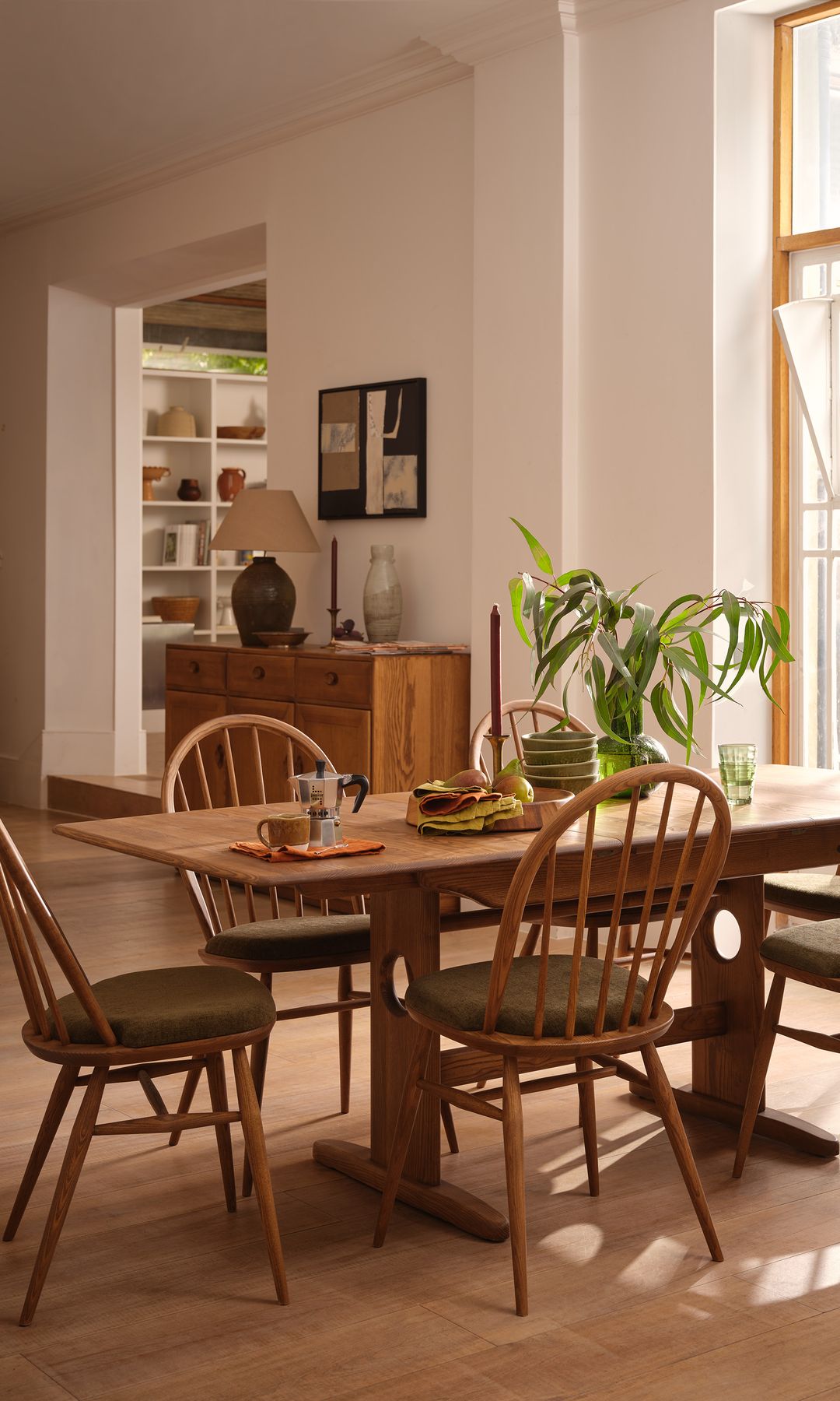 Comedor de estilo nórdico con mesa y sillas de madera, planta, aparador de madera con lámpara de sobremesa