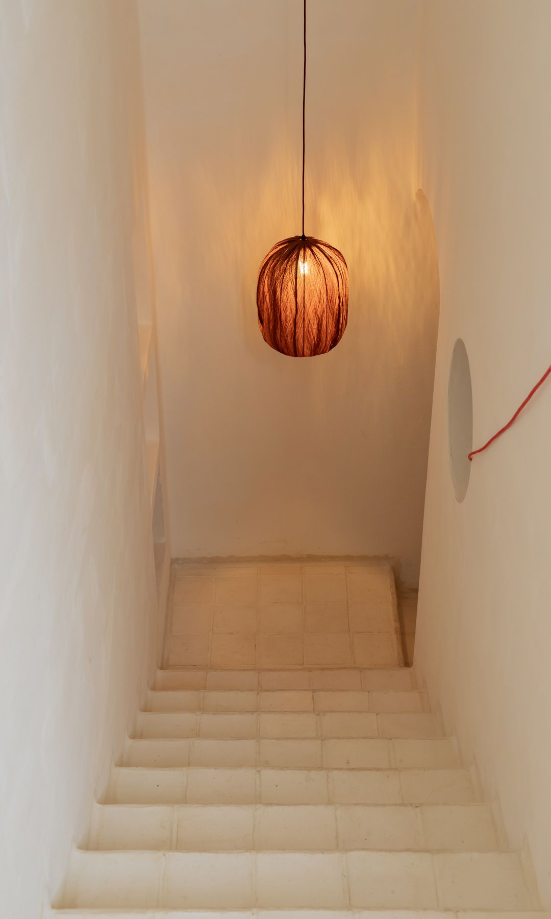 Subida de la escalera, paredes encaladas, lámpara de techo de fibras vegetales