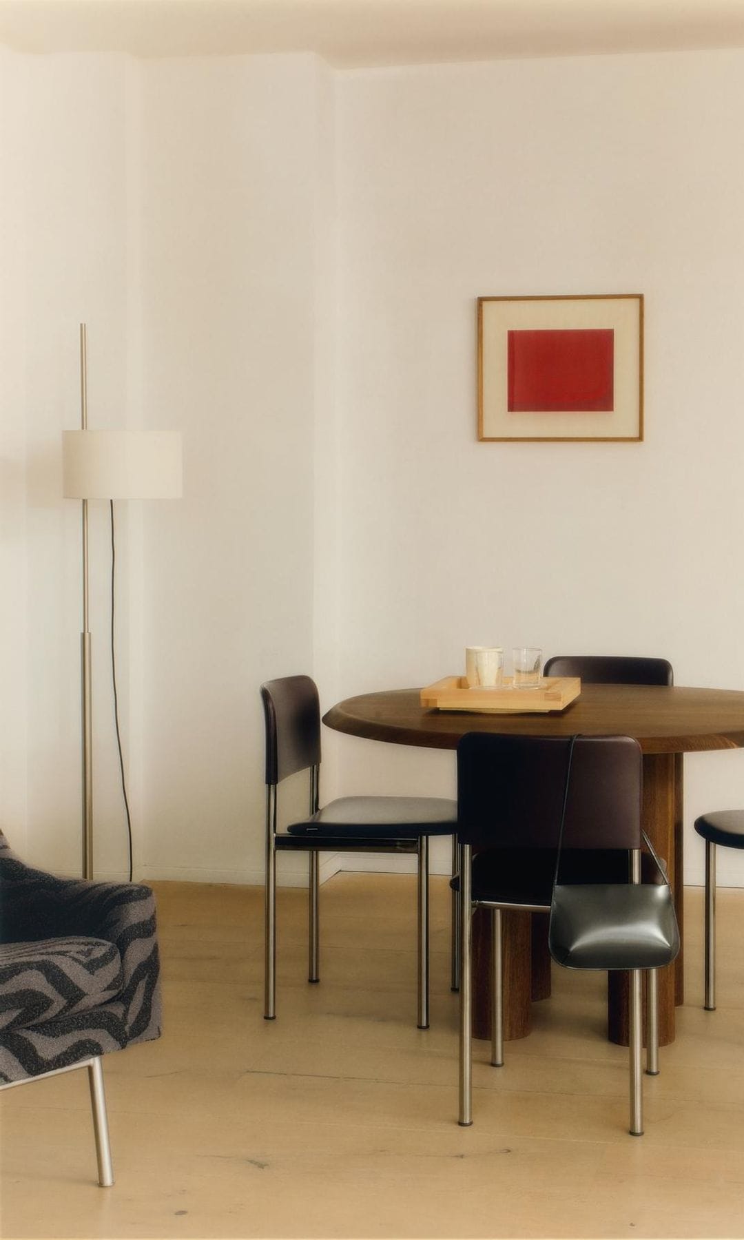 Comedor con mesa redonda de madera, sillas negras con estructura metálica, lámpara de pie