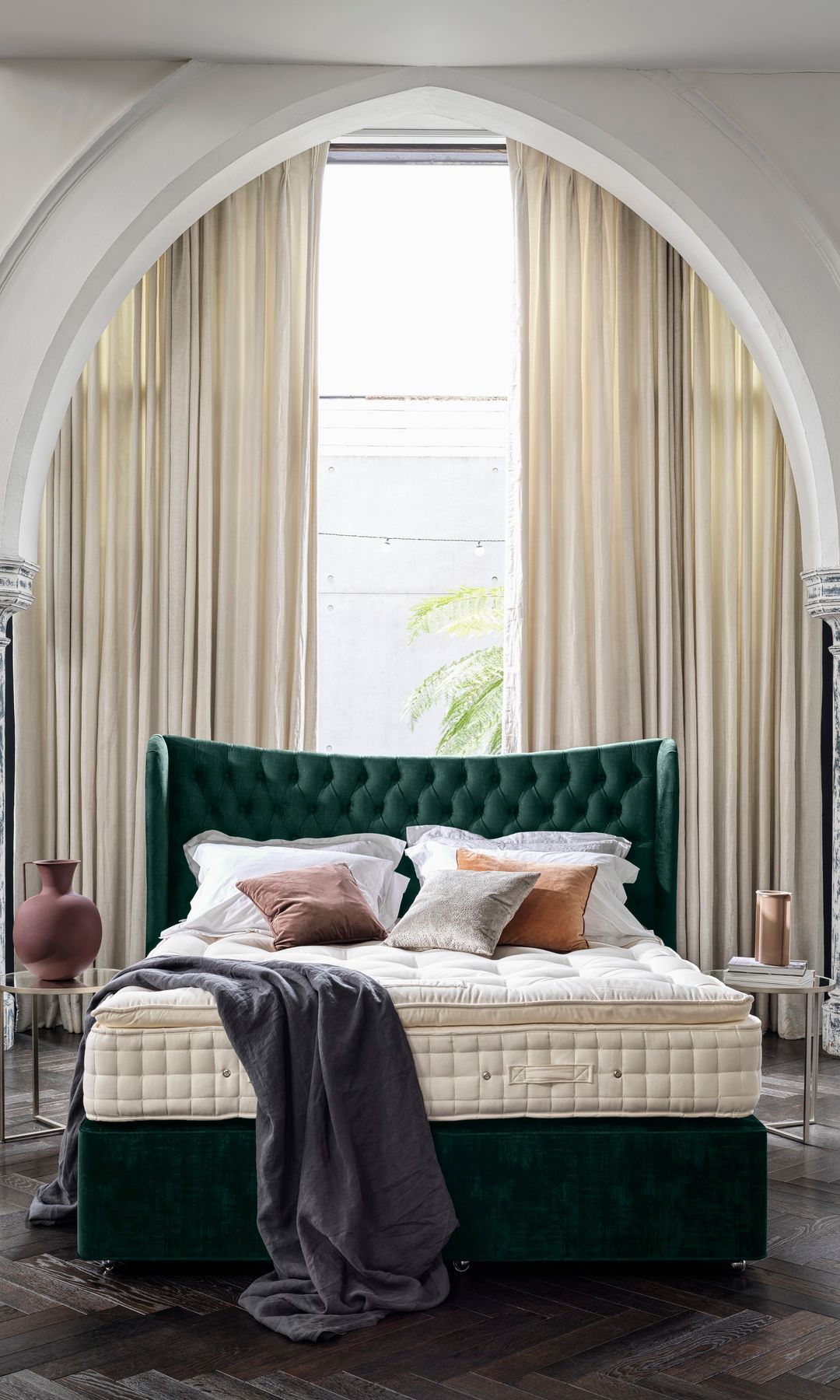 Dormitorio con cabecero con capitoné verde y colchón sin sábanas, arco en la pared
