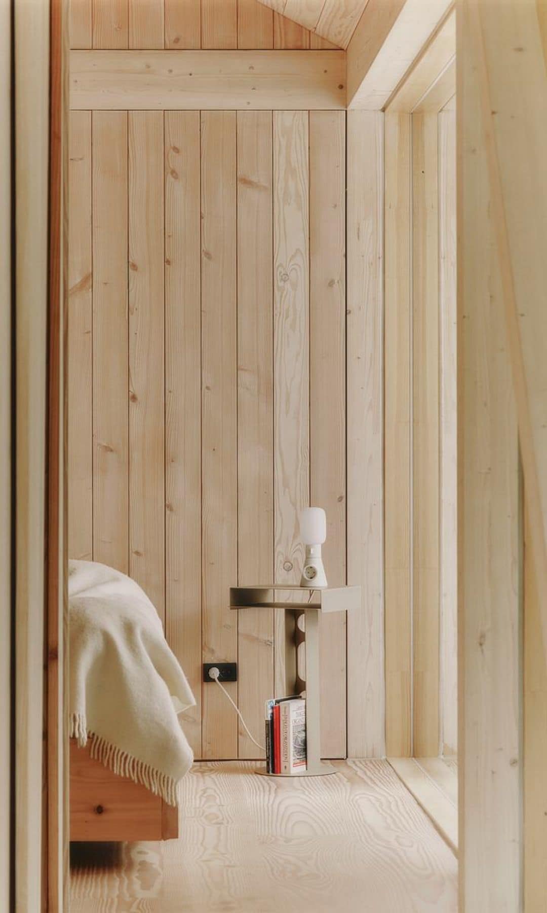Dormitorio con paredes de madera, mesita de noche, enchufe en la pared, lámpara de sobremesa blanca con enchufe integrado