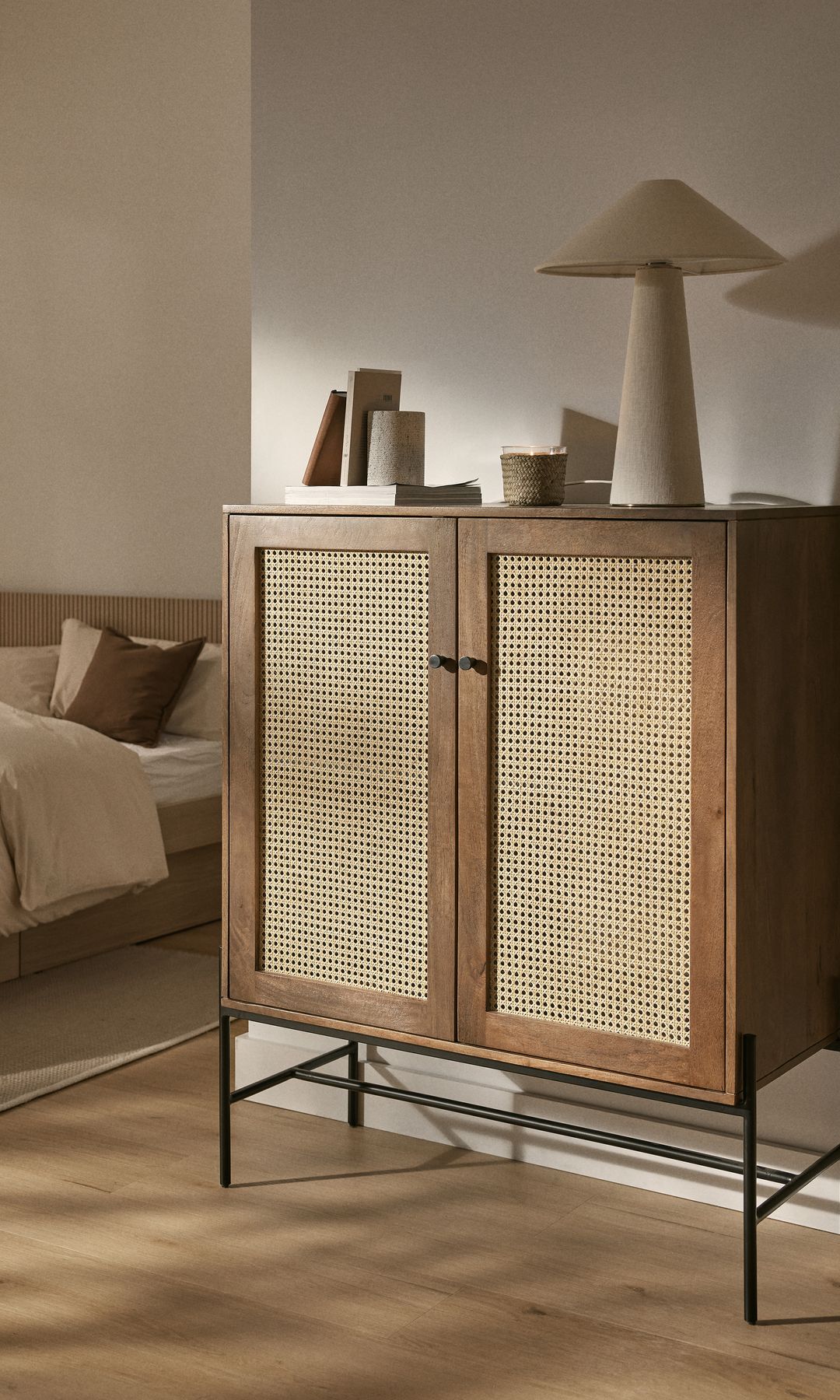 Dormitorio en tonos cálidos, suelo de madera, aparador alto con puertas de rejilla, lámpara de sobremesa, adornos 