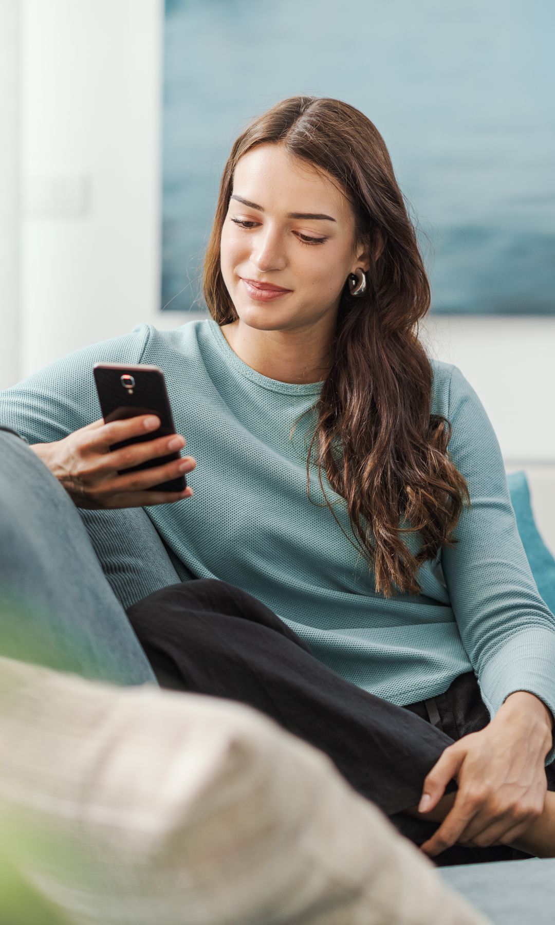 Una mujer mirando el móvil sentada en su sofá