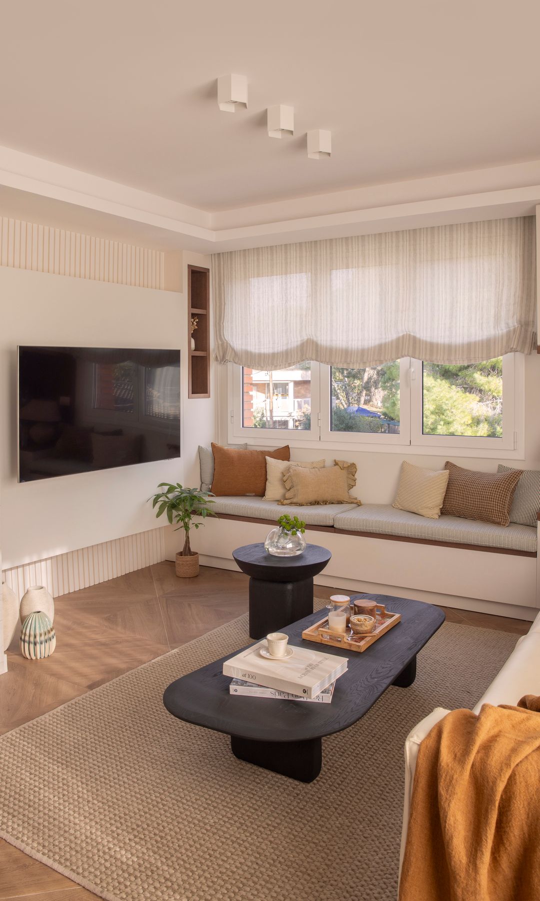 Salón con chimenea y televisión colgada en la pared, con banco bajo la ventana y estores 