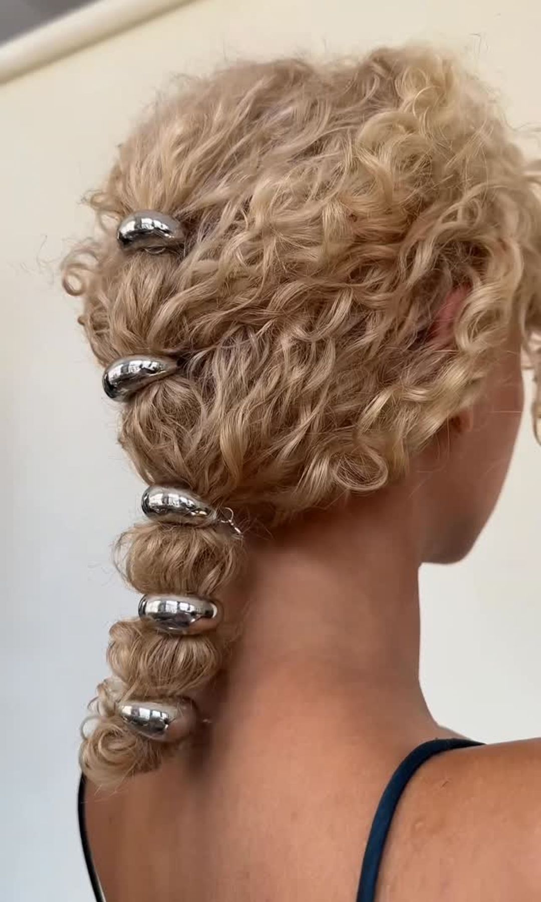 Peinado recogido para pelo rizado con accesorios metálicos sobre melena rubia