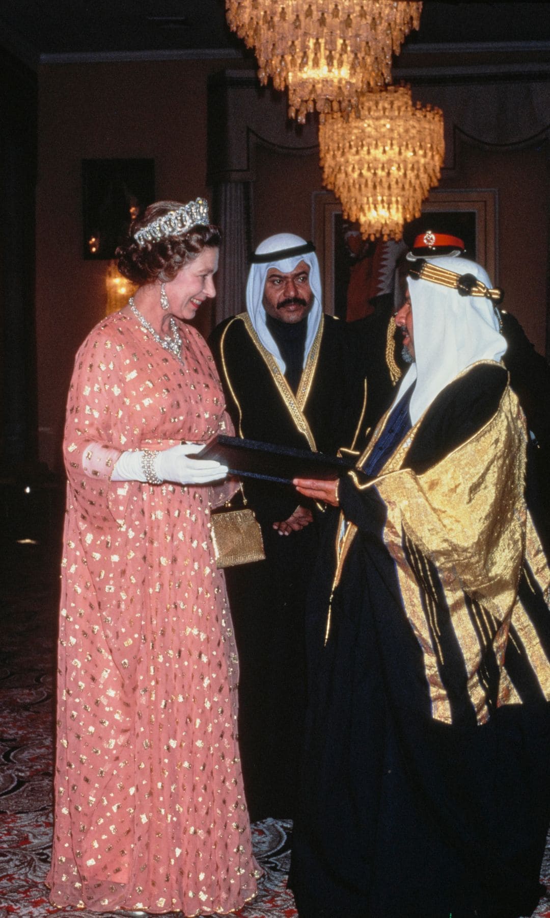 British Royal Queen Elizabeth II, wearing a salmon pink outfit with gold detail and white gloves, and the Grand Duchess Vladimir Tiara, receives a gift from the Emir of Bahrain, Isa bin Salman Al Khalifa (1931-1999), at the Al-Qudaibiya Palace in Manama, Bahrain, 15th February 1979. The Queen is on an 18-day tour of the Gulf States. (Photo by Tim Graham Photo Library via Getty Images)