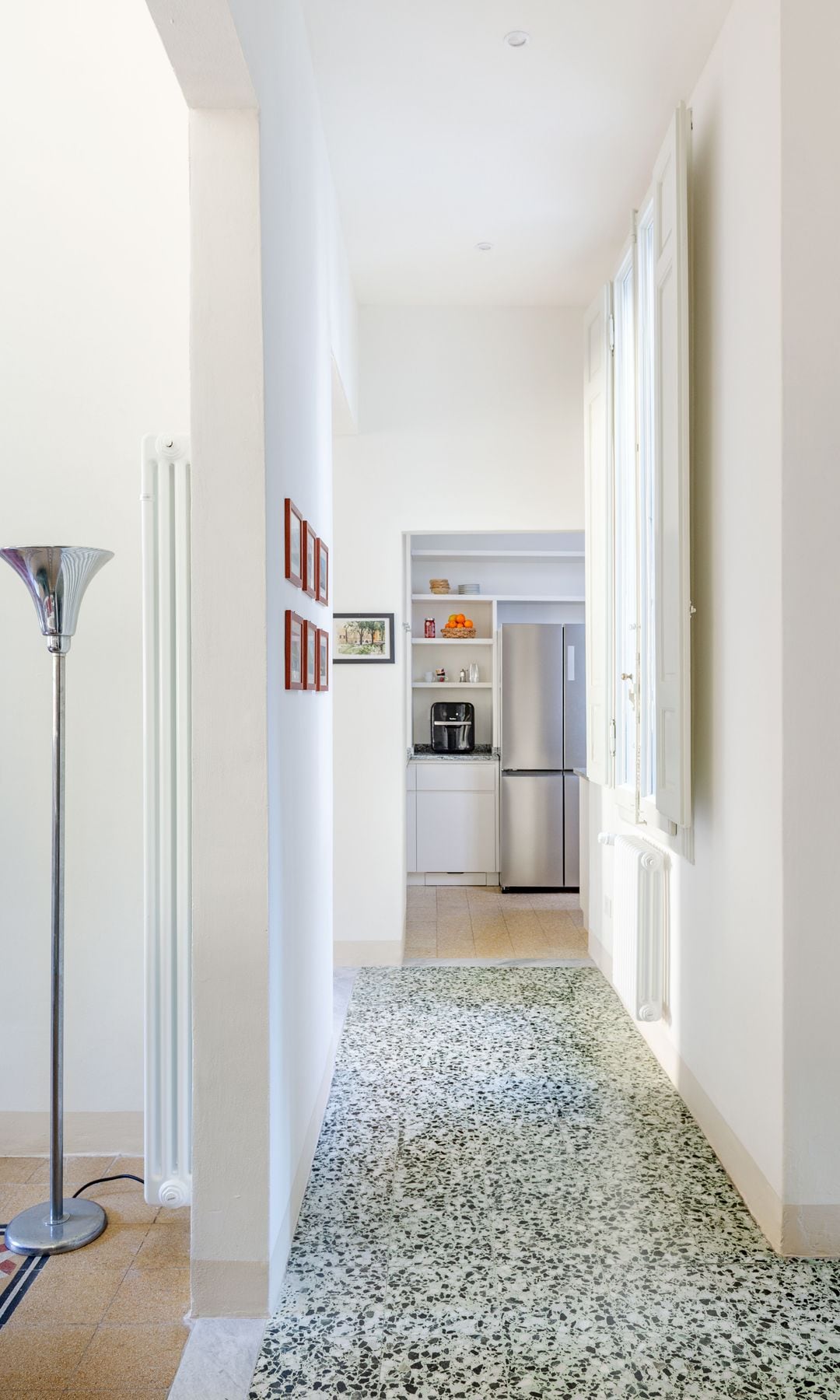 Pasillo con suelo terrazo original de color verde, ventanas con marco de madera, cuadros en la pared 