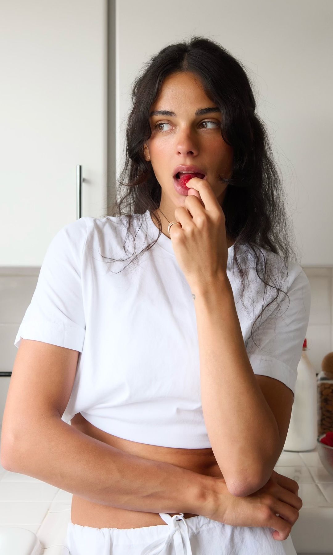 Una chica con camiseta blanca en la cocina comiendo frambuesas