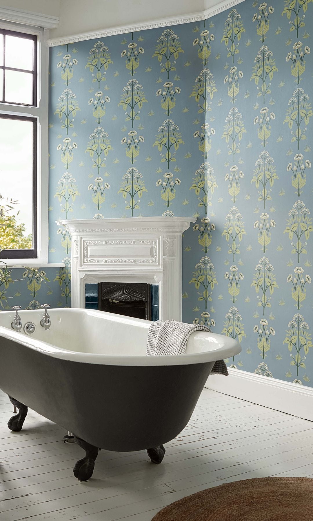 Bañera exenta, suelo de madera pintado de blanco, chimenea y papel pintado con motivos vegetales en azul y verde