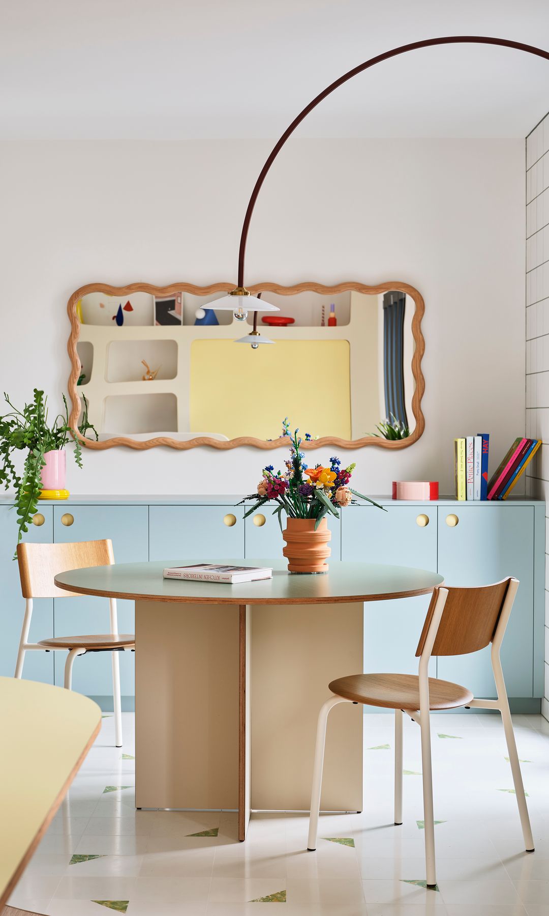 Comedor con mesa redonda, sillas de madera, espejo con marco curvo de madera, aparador en azul claro, lámpara de pie en arco, jarrón con flores