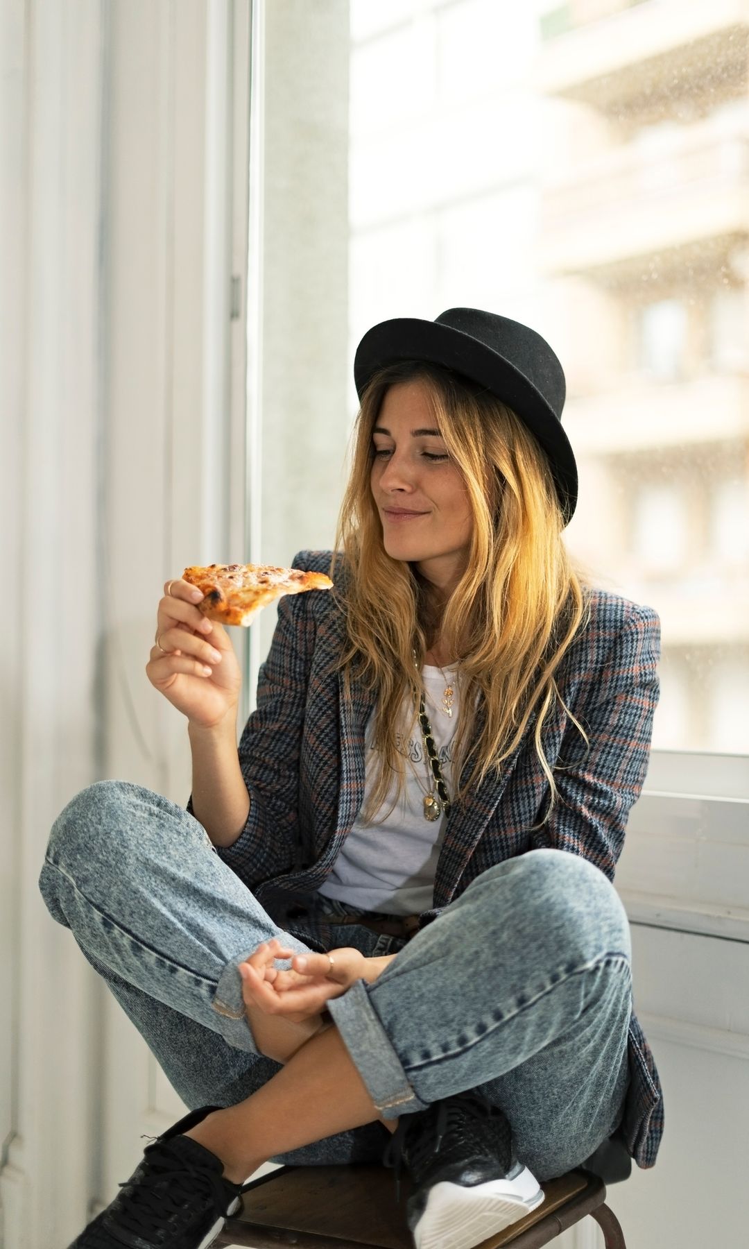 Mujer joven con sombrero comiendo pizza en su casa